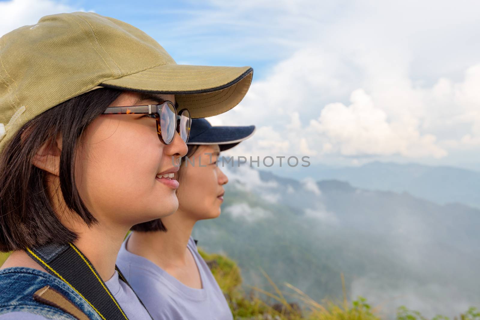 Face two young women hiker, mother and daughter smiling happily while looking beautiful landscape nature of mountain range and sky at Phu Chi Fa Forest Park, Chiang Rai, Thailand