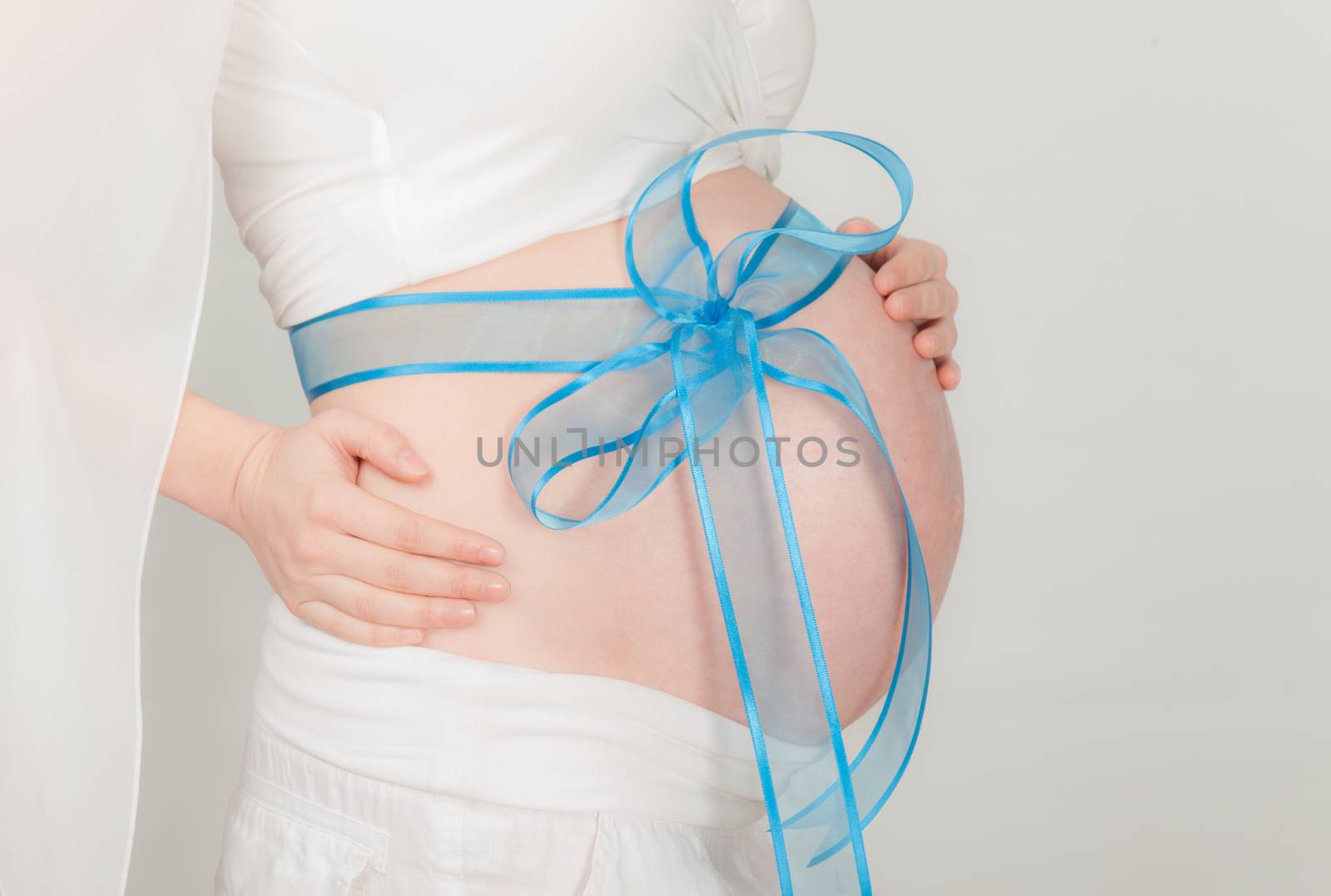A close-up of pregnant woman abdomen with blue ribbon around. Gray background with copy space.
