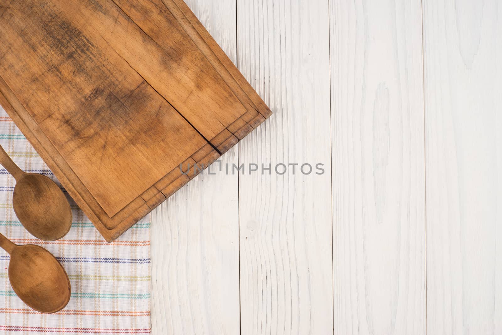Cutting board and a spoon on a kitchen napkin on old wooden tabl by DGolbay