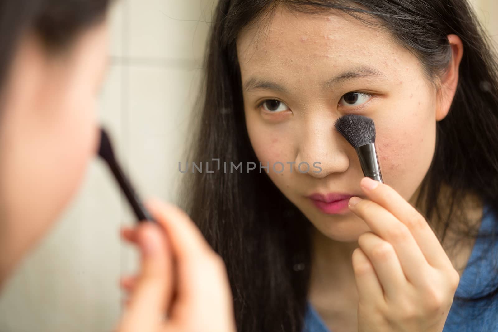 Chinese teenager putting on makeup with brush in front of mirror