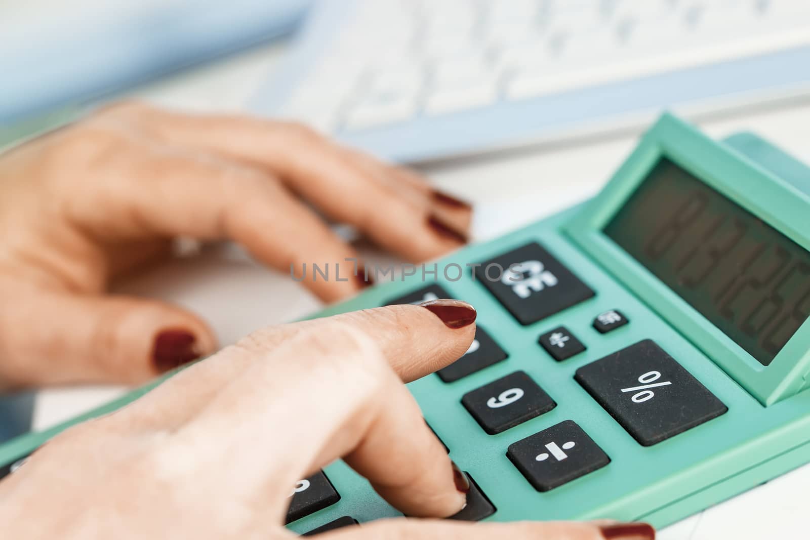Close-up portrait of red nails businesswoman hand while using calculator.