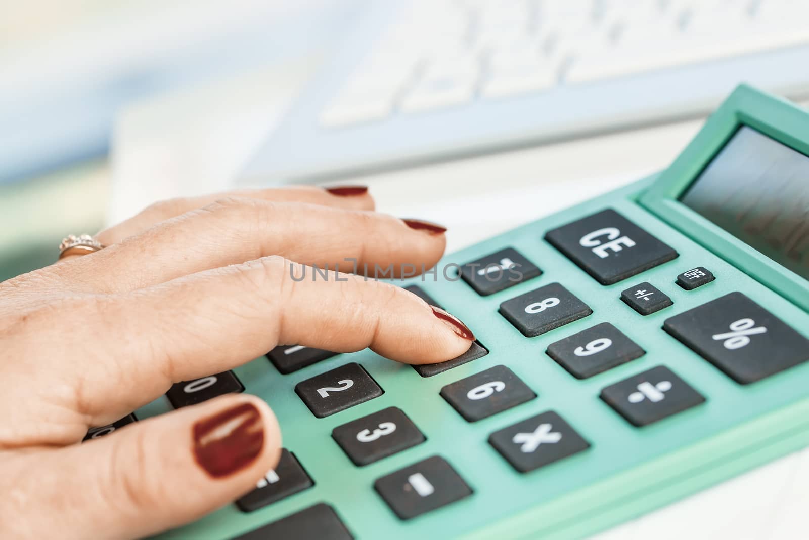 Close-up portrait of red nails businesswoman hand while using calculator.