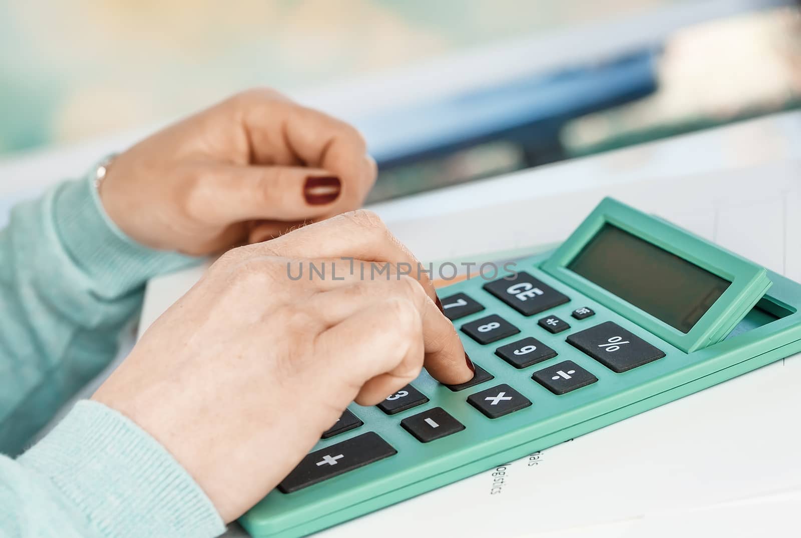 Close-up portrait of red nails businesswoman hand while using calculator.