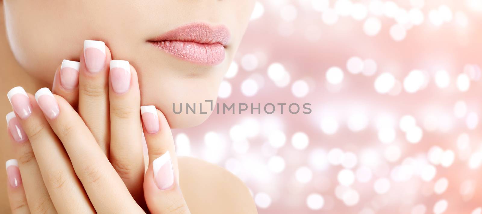 Beautiful young woman with healthy skin and french manicure on an abstract background with blurred lights