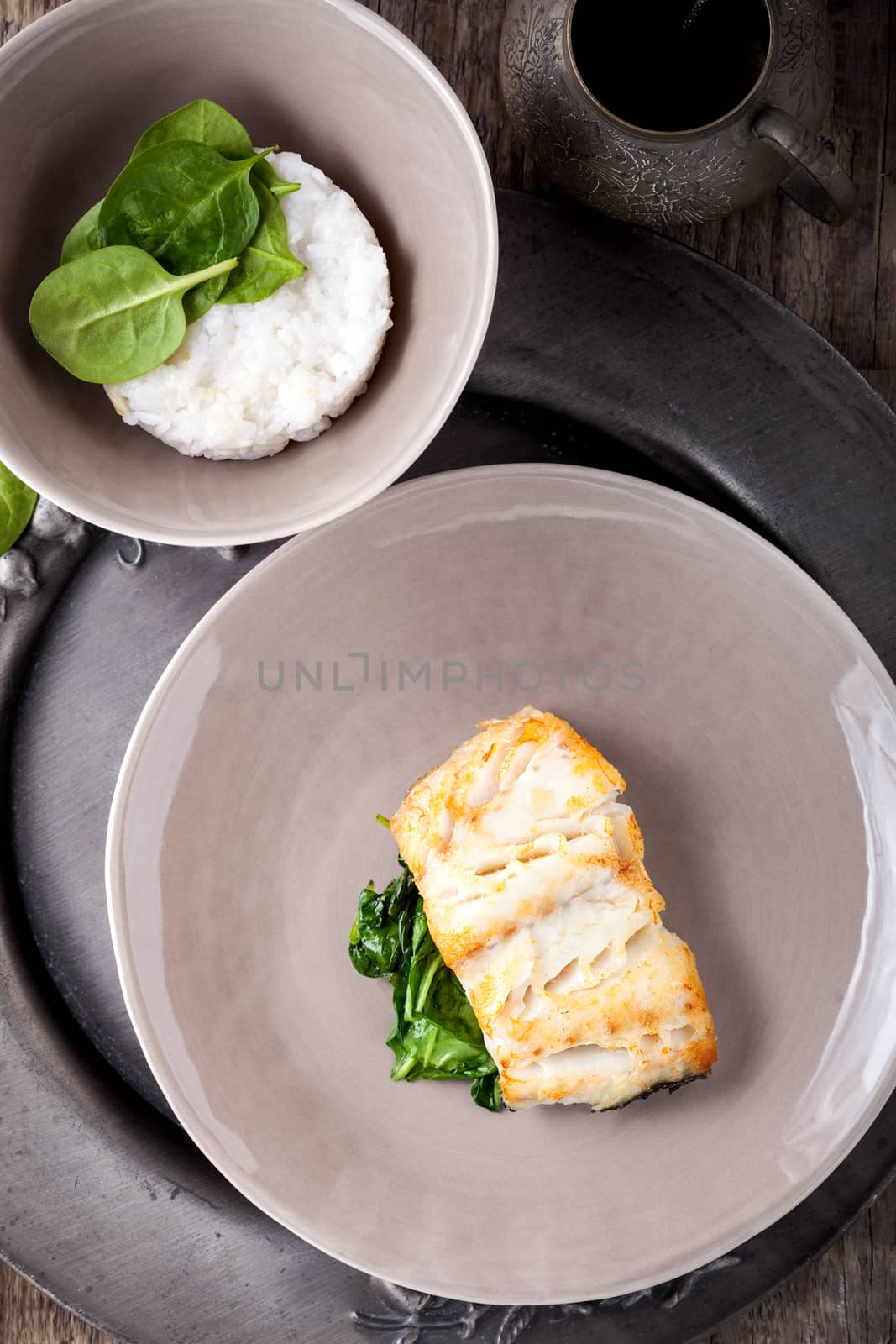 Fried cod fillets and spinach served on a wooden surface