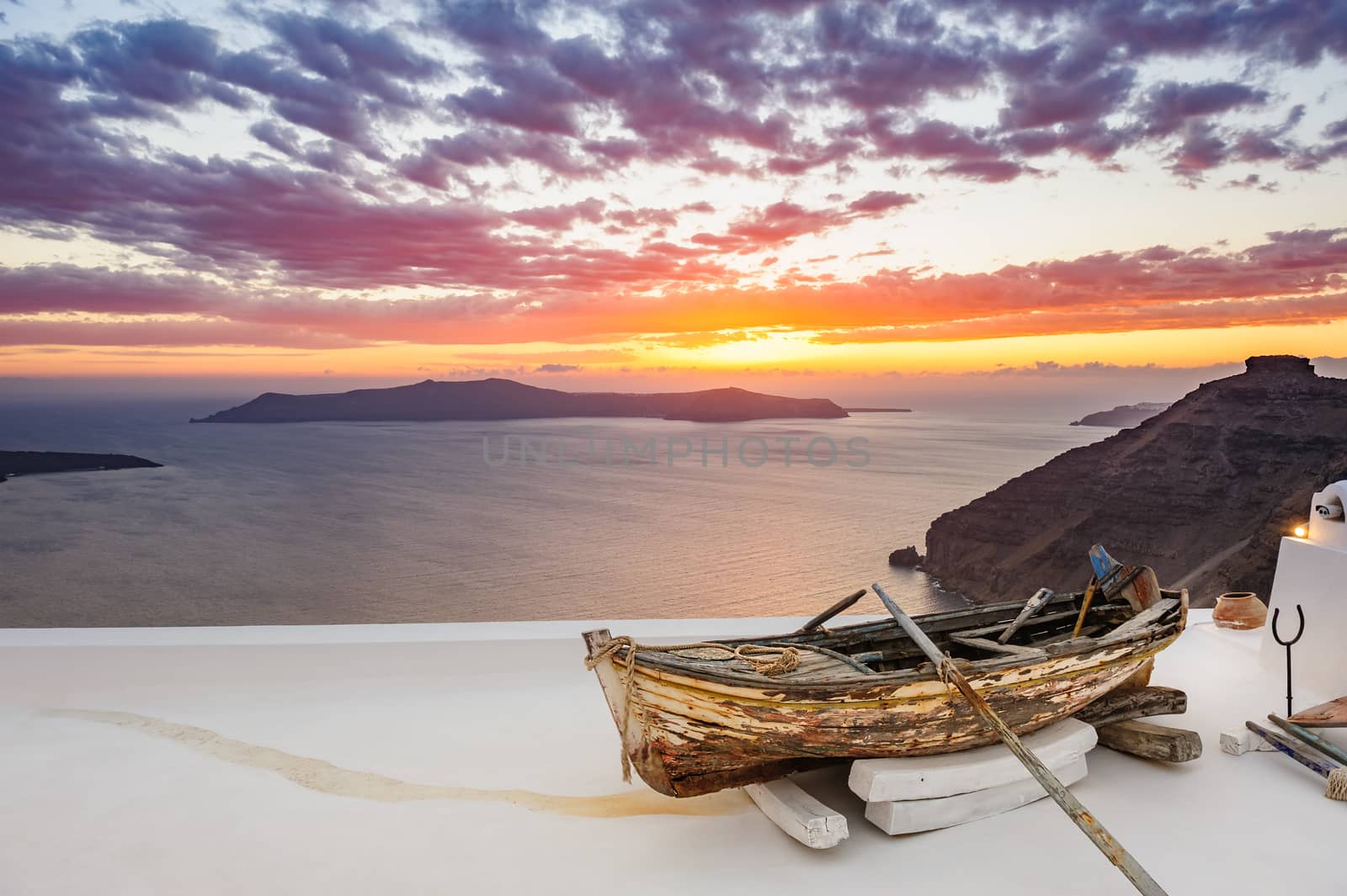 Old wooden fishermans''s boat on roofof house in Firostefani village with typical white architecture, Santorini island, Greece, during sunset over sea.