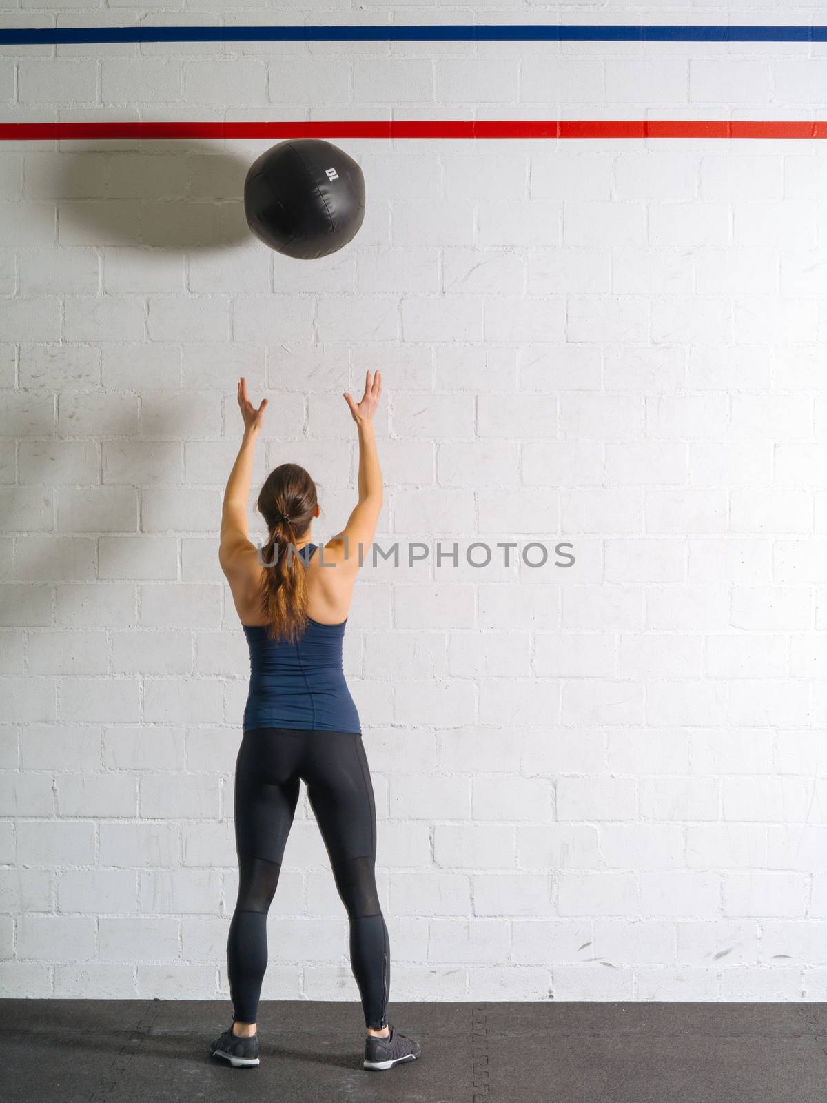 Photo of a woman exercising by throwing a medicine ball up against a wall in a gym.

