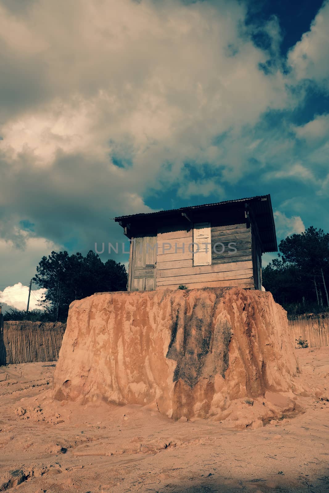 Lonely old wooden house on earth mound after scoop soil for clearance at Da Lat, Viet Nam make funny scene