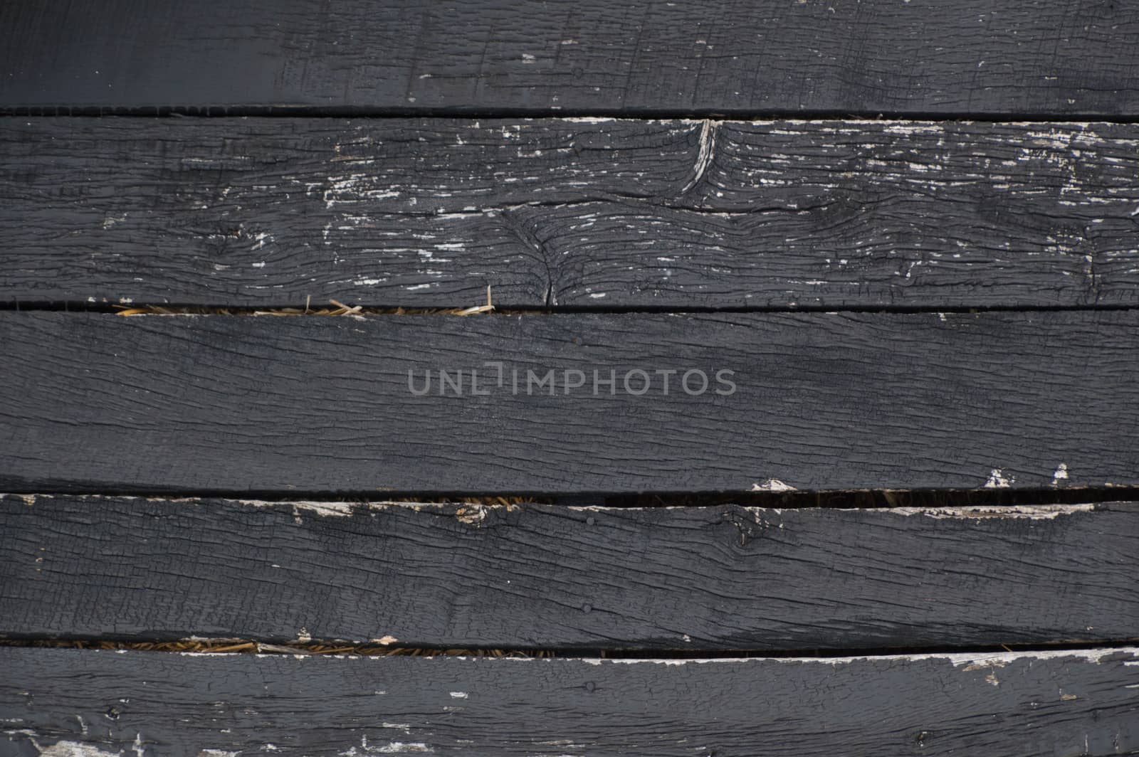 Black peeling, crackled, weathered horizontal wooden barn boards with straw