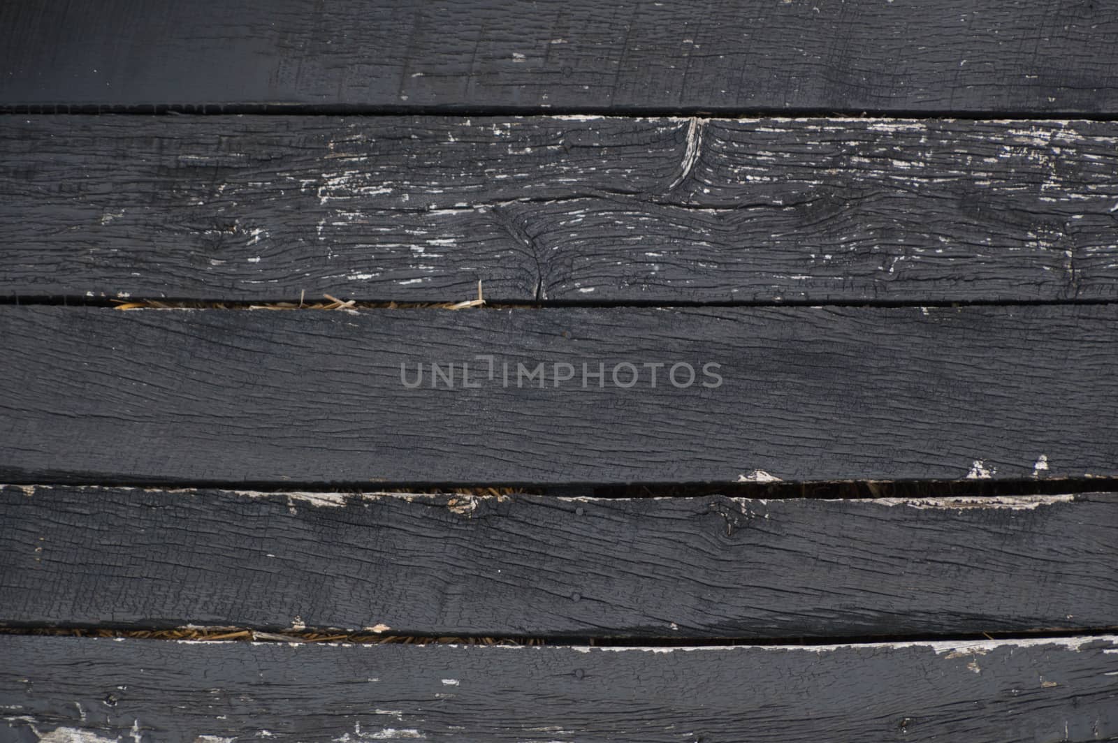 Black peeling, crackled, weathered horizontal wooden barn boards with straw