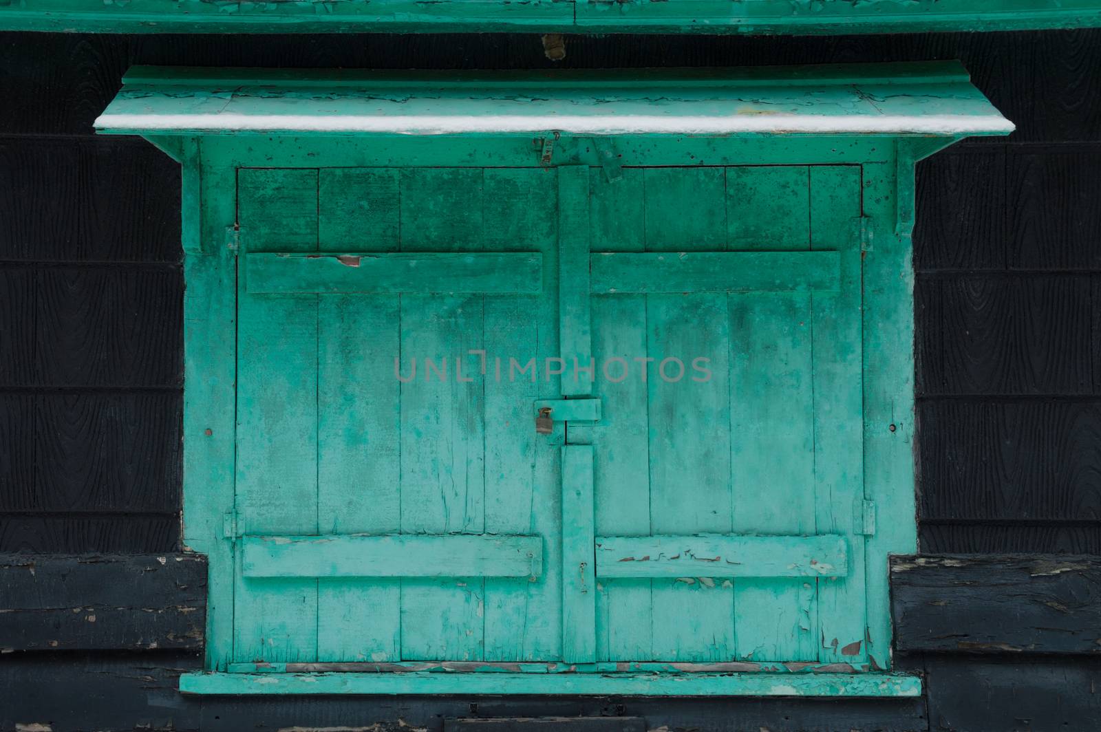 Grungy faded green mildewy shuuters with snow on a waterfront cottage.  Locked on a black cottage in winter