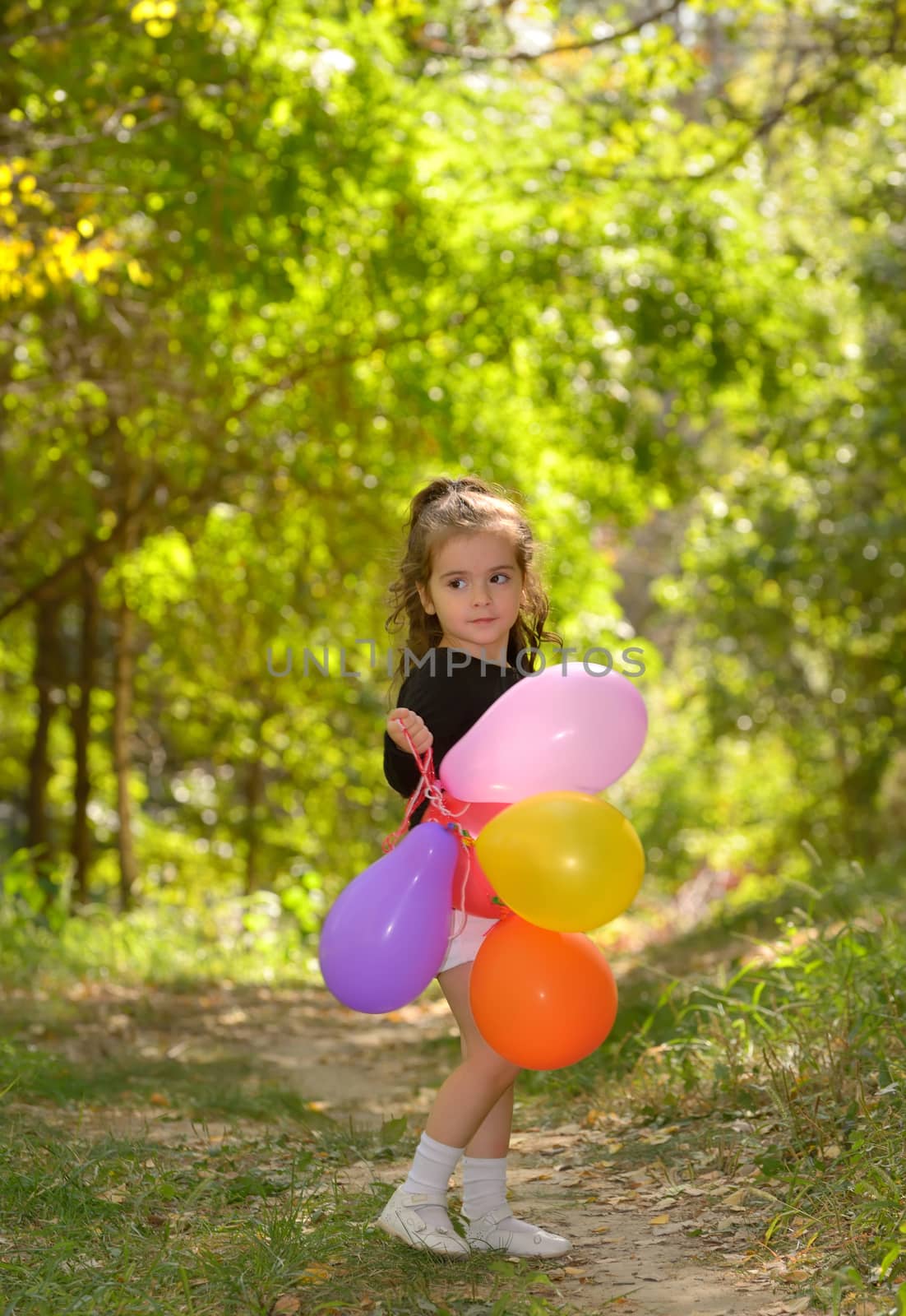 Little girl with colorful balloons in forest