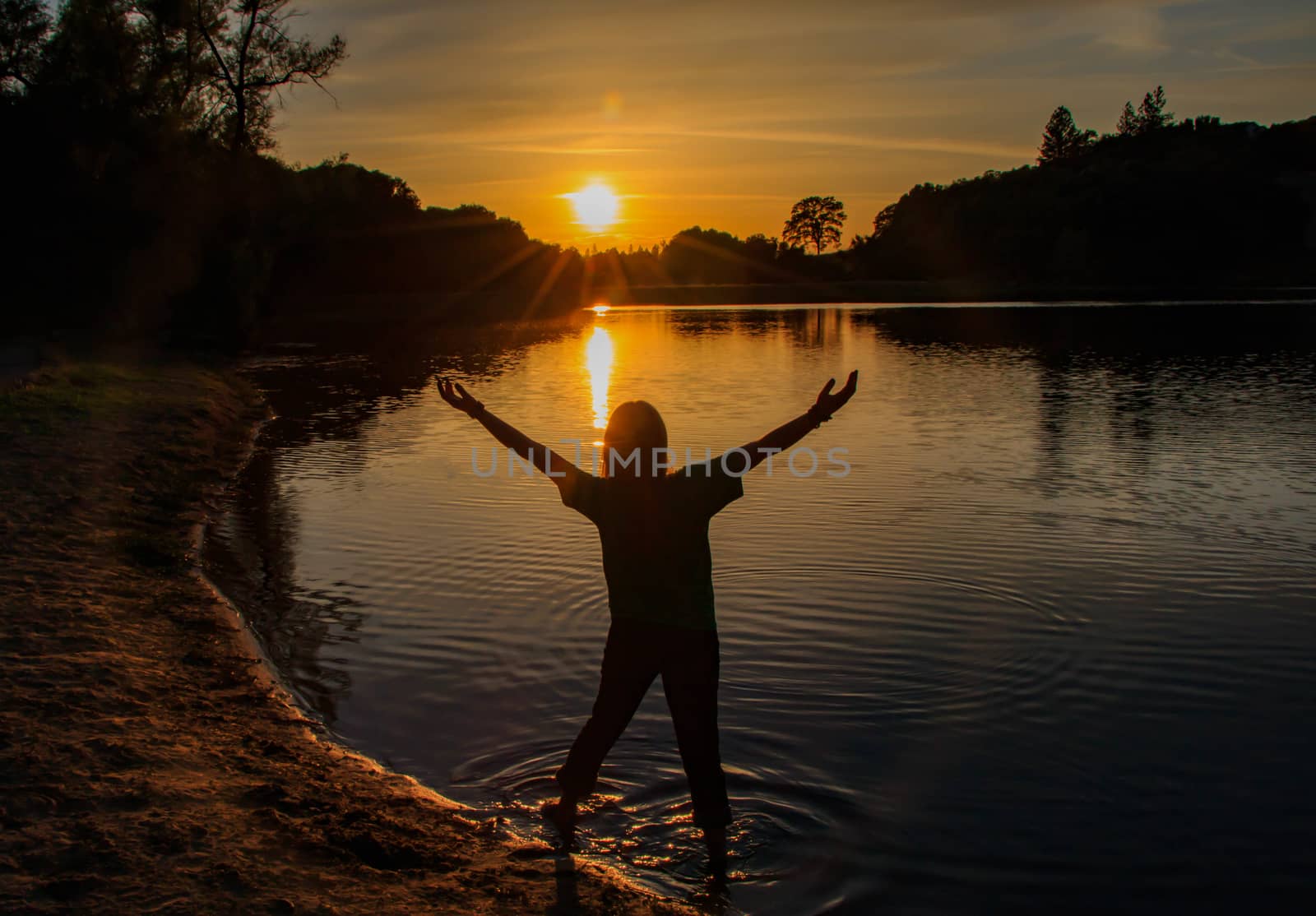 Young Girl Watching the Sun Set With Hands Raised High