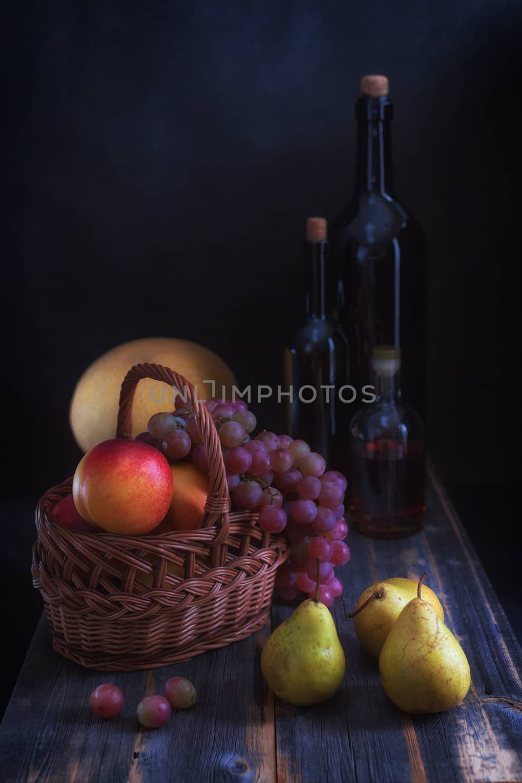 Fruit in a basket, a melon and bottles with wine on old wooden boards