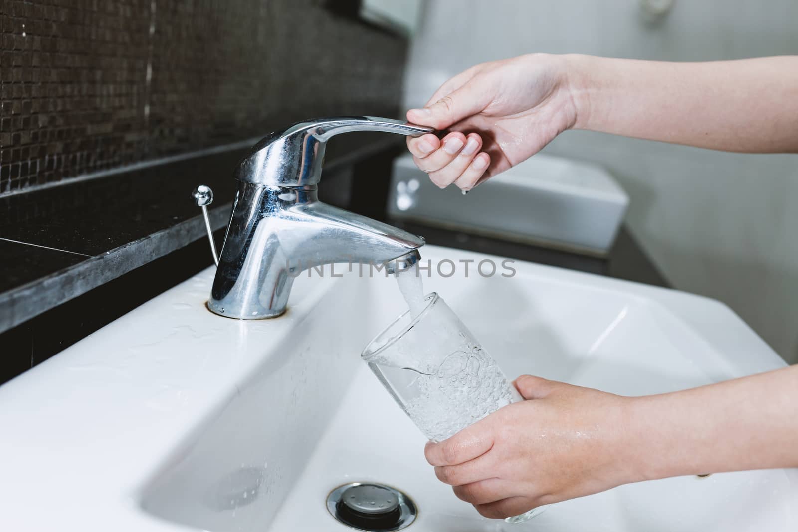 Woman filling a glass of water from a stainless steel or chrome by nopparats