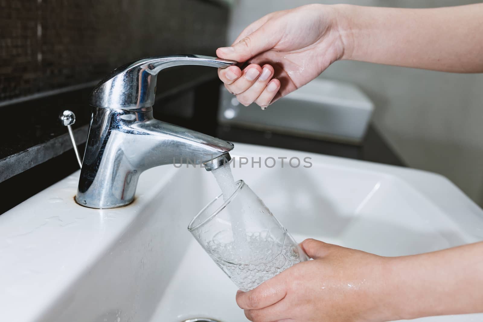 Woman filling a glass of water from a stainless steel or chrome by nopparats
