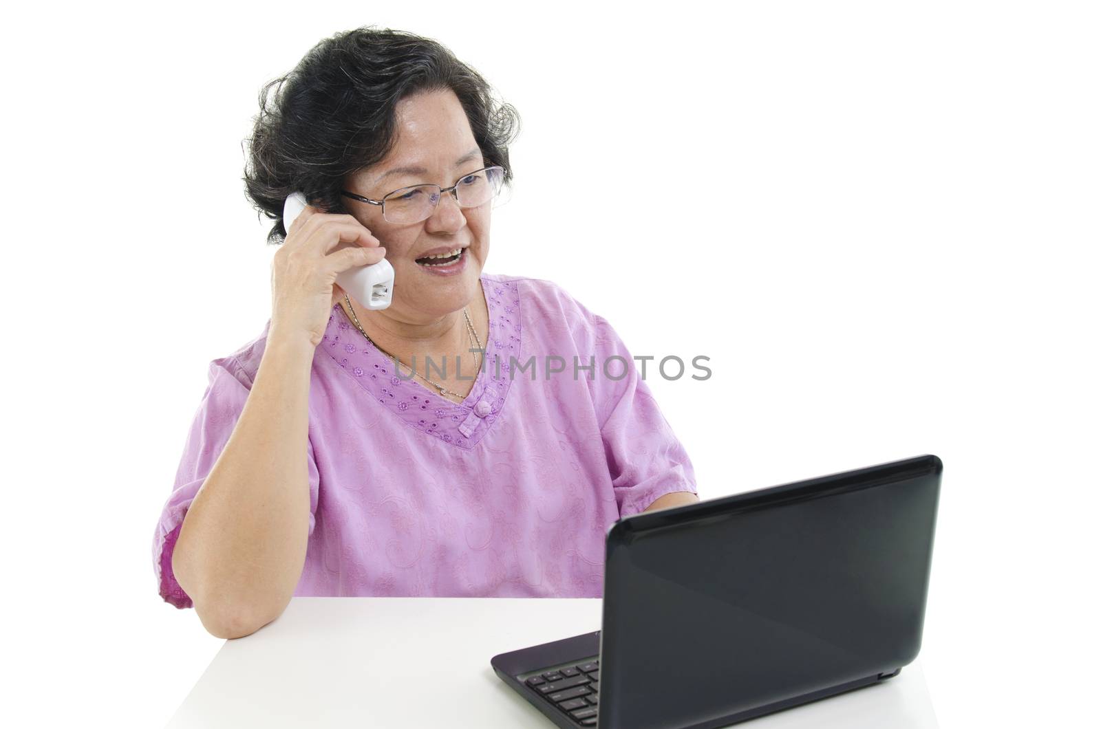 Portrait of modern 60s Asian senior adult woman using laptop computer and calling on telephone, isolated on white background.