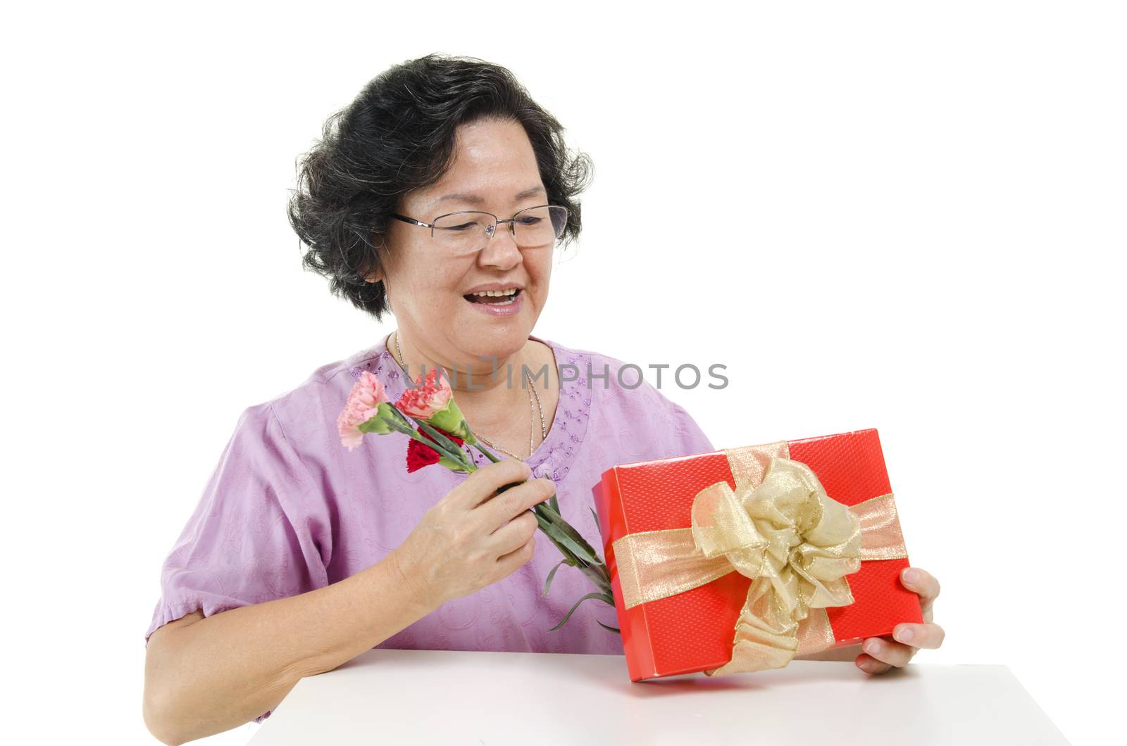 Happy mothers day concept. Portrait of 60s Asian senior adult woman receiving gift box and carnation flower from her child, isolated on white background.