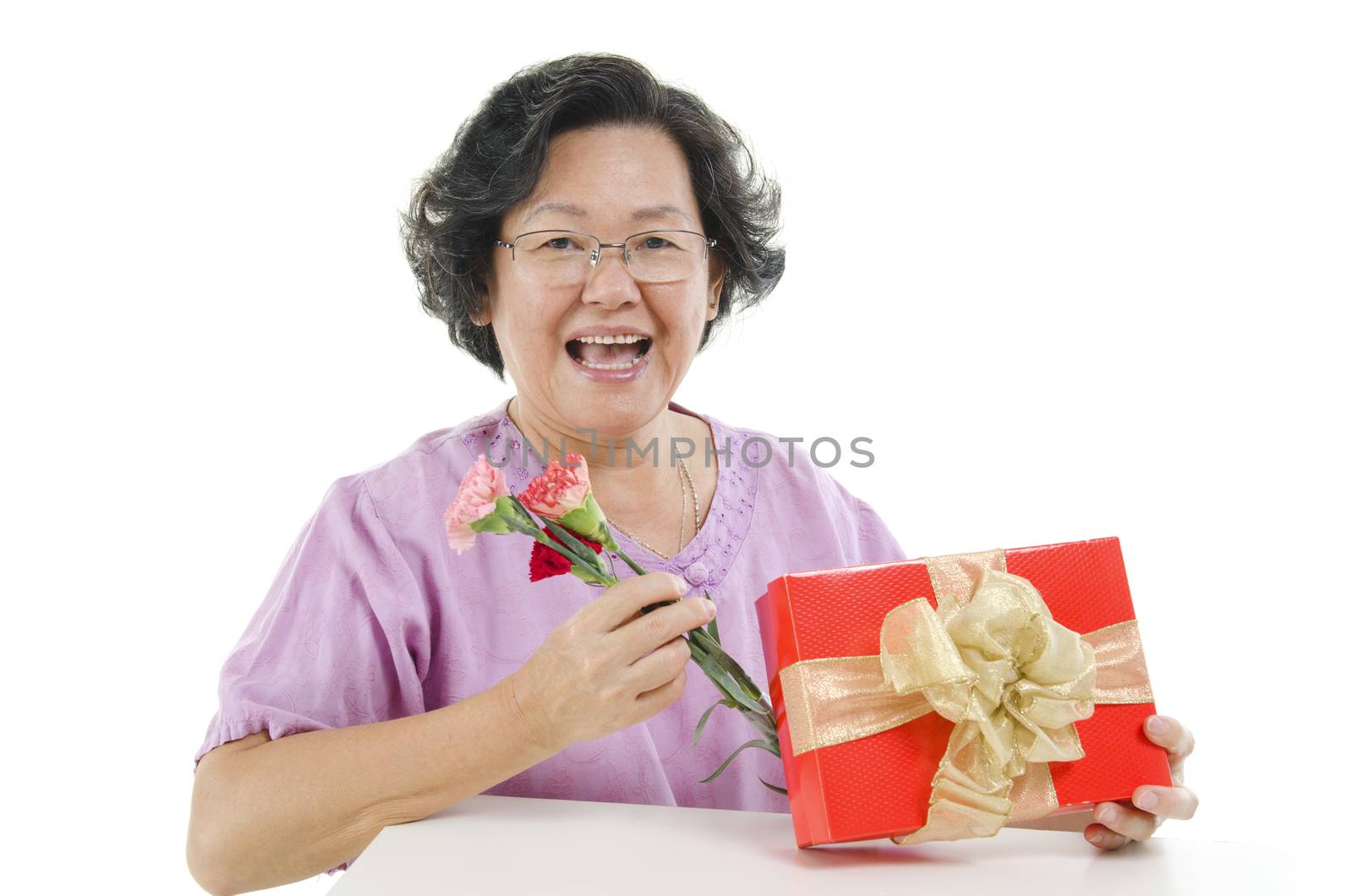 Portrait of happy 60s Asian senior adult woman receiving gift box and carnation flower on mothers day, isolated on white background.