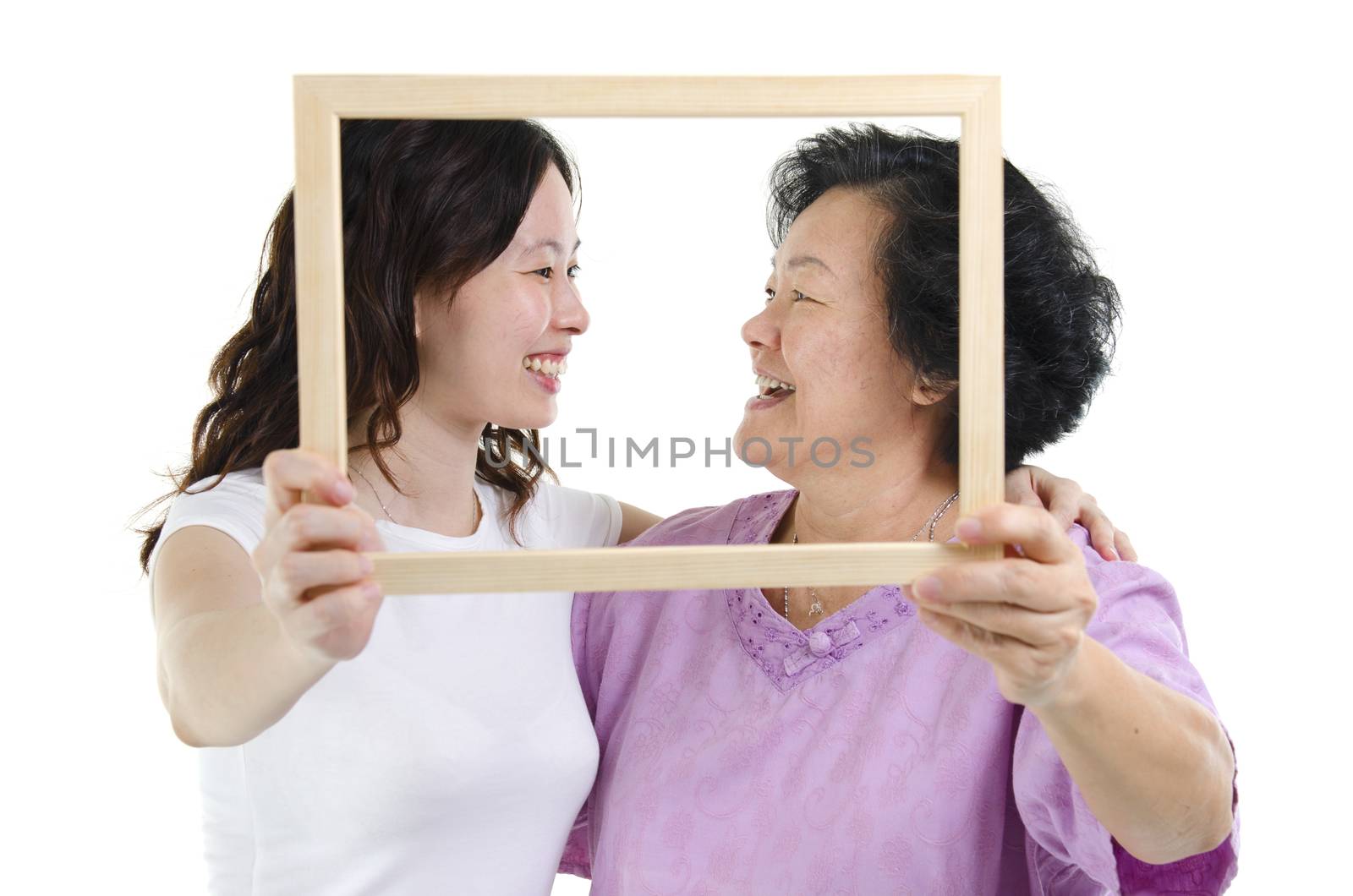 Portrait of Asian senior mother and adult daughter hands holding an empty photo frame, looking at each other, isolated on white background.