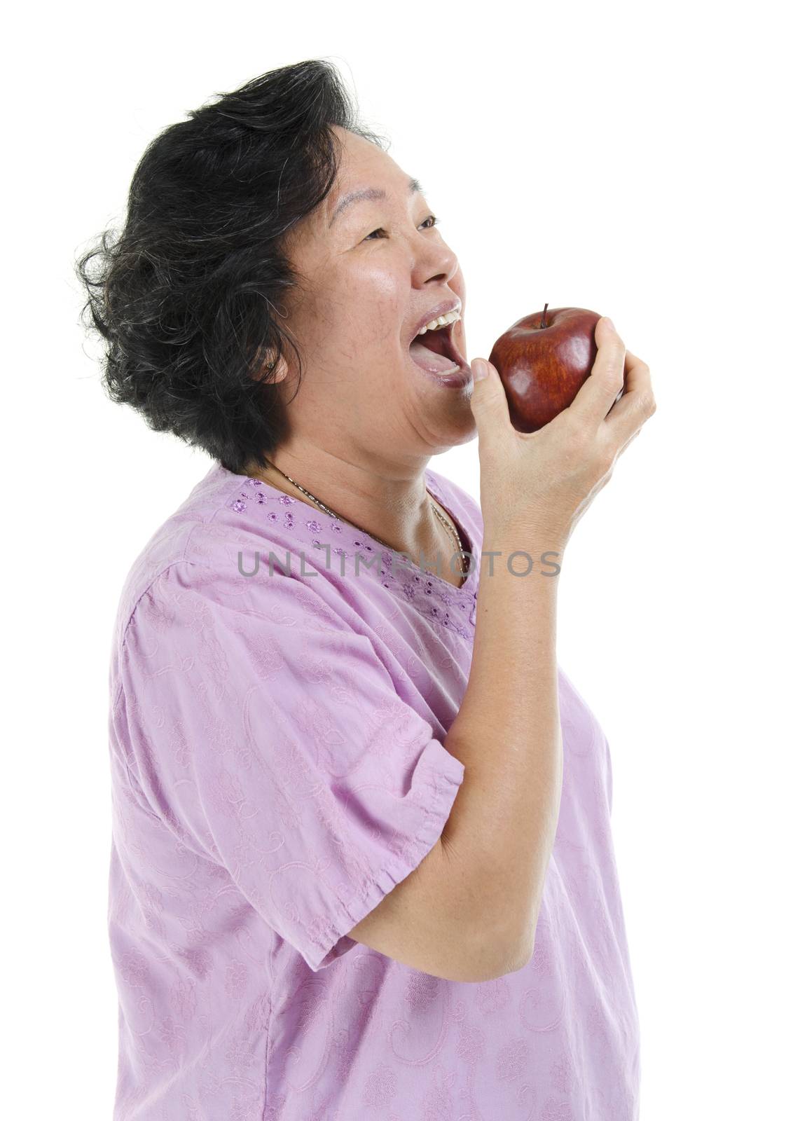 Elderly healthy diet. Portrait of happy 60s Asian senior adult woman smiling and eating an apple, isolated on white background.