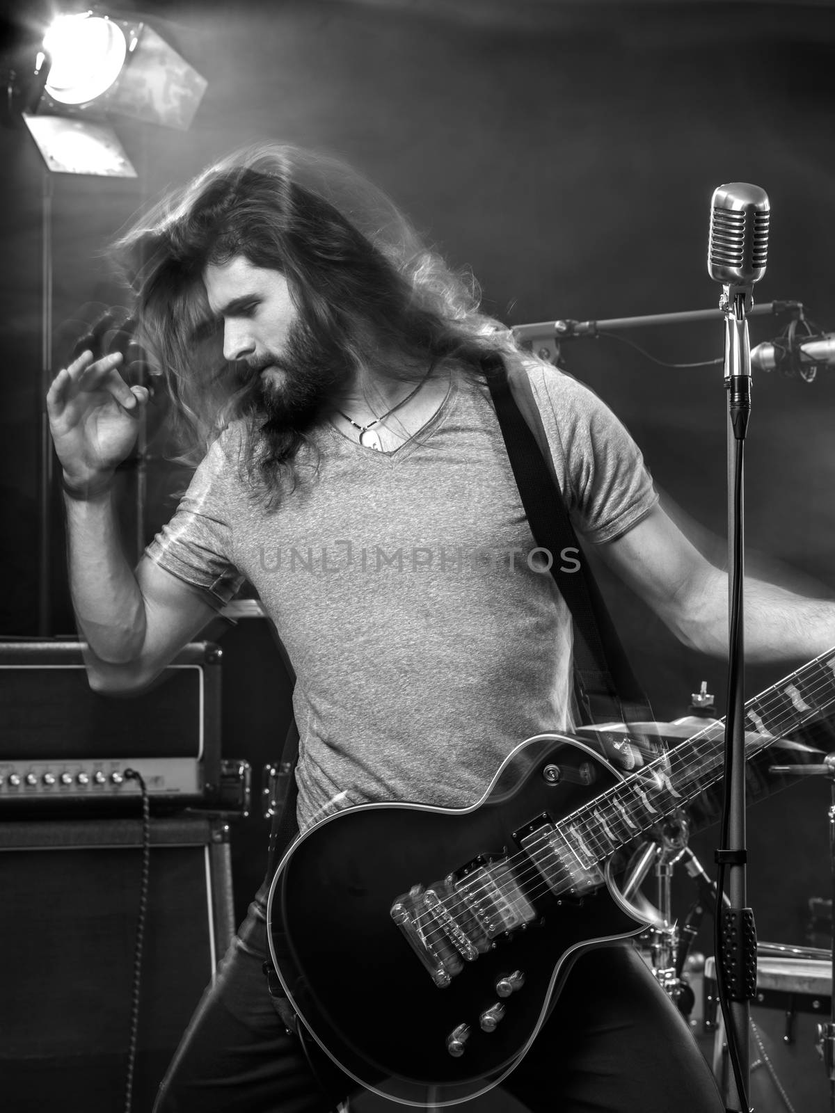 Photo of a young man playing electric guitar on stage with motion blur.