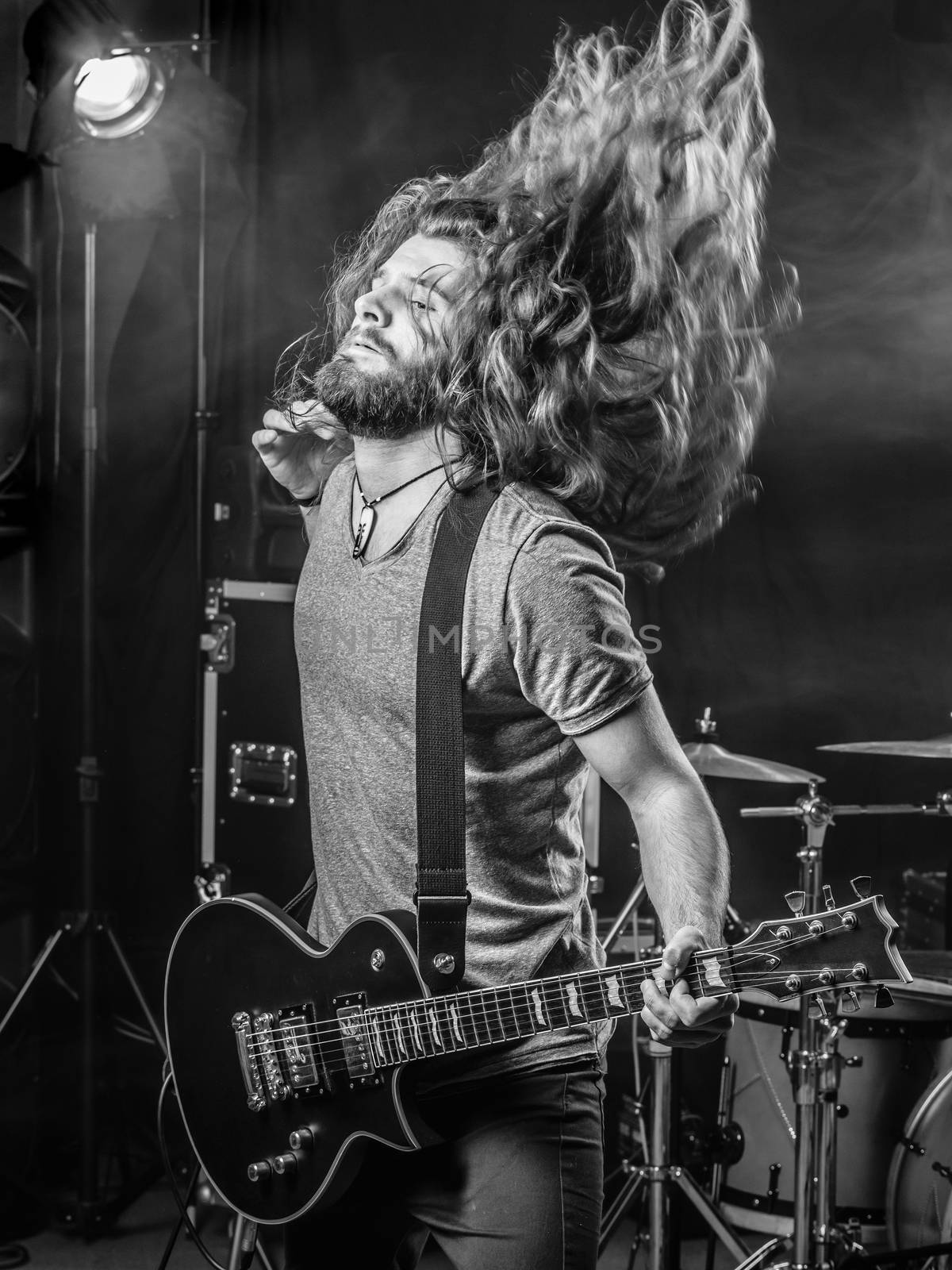 Photo of a young man playing electric guitar on stage and tossing his long hair around.