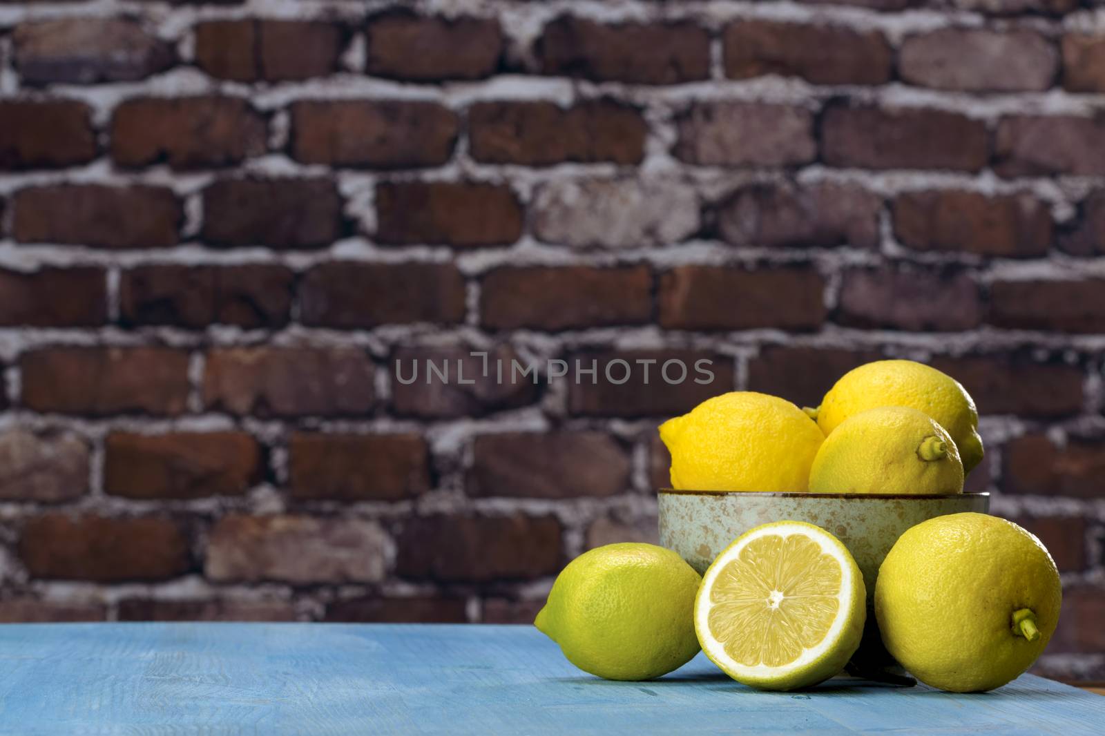Ripe yellow lemons arranged in a gray bowl. In the background of raw red brick wall.