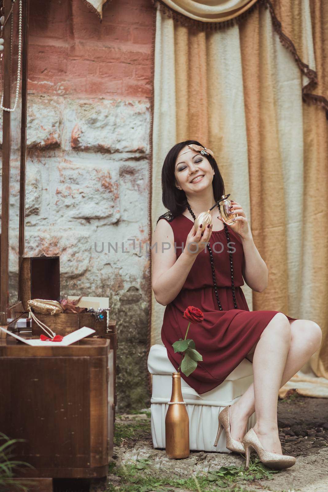 retro girl sitting at a dressing table and holding bottle of perfume in hand