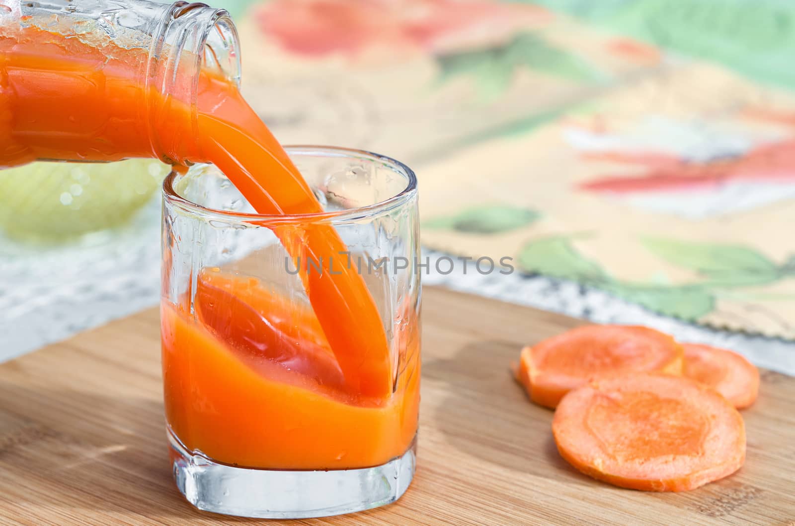 Fresh carrot juice is poured from a bottle into a glass, which stands on the table. Selective focus.