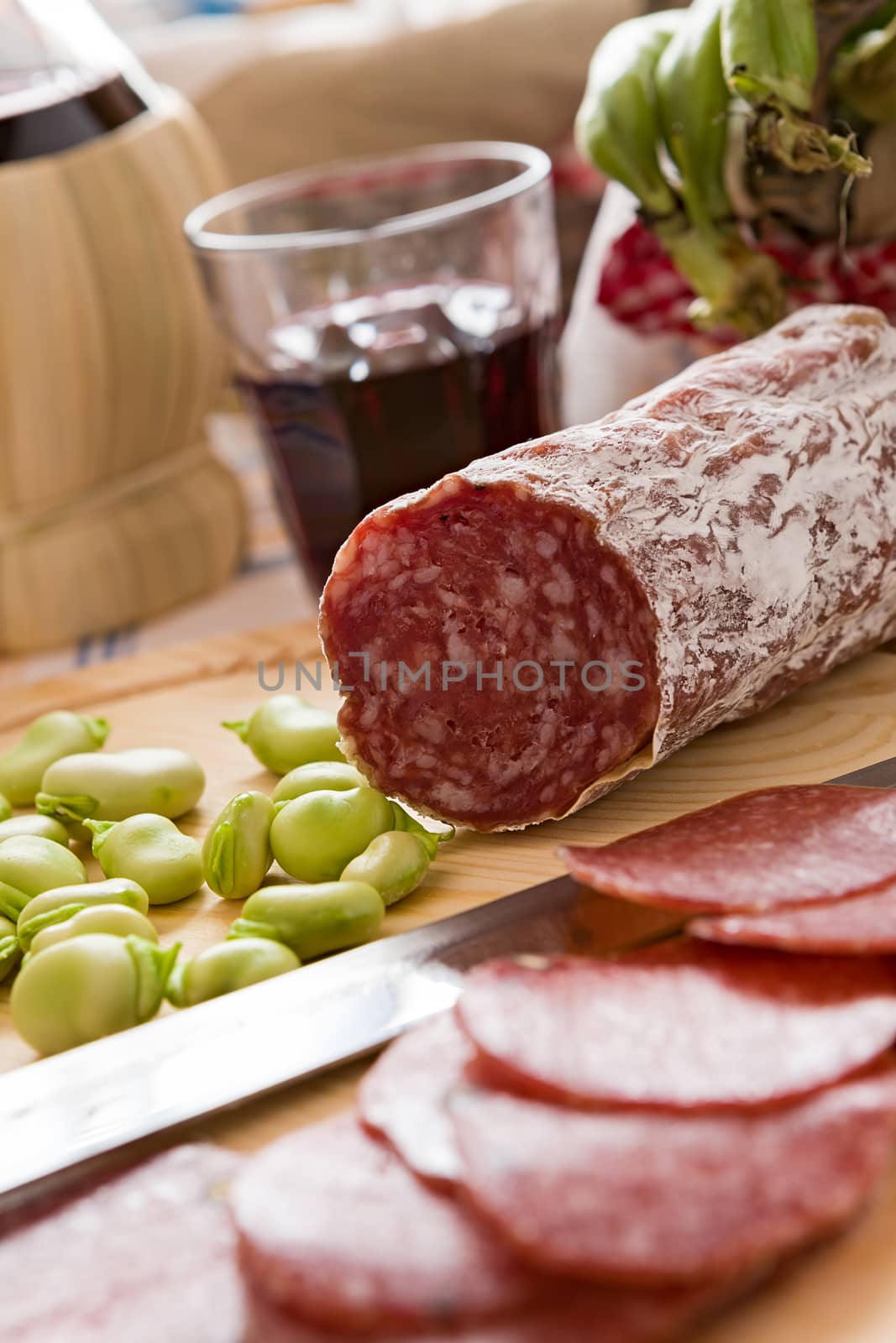 Close up of Italian salami with broad bean over a chopping board and a glass of red wine