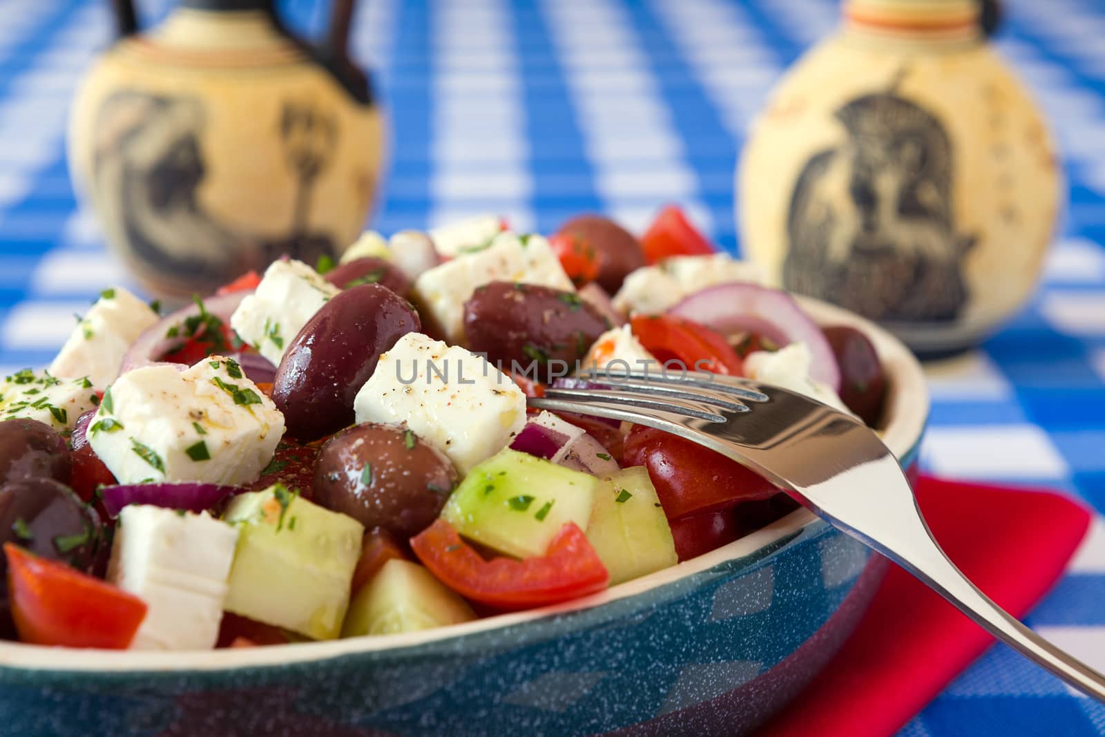 Close up of greek salad with feta cheese tomatoes cucumber olives and onions with greek amphorae over a red napkin