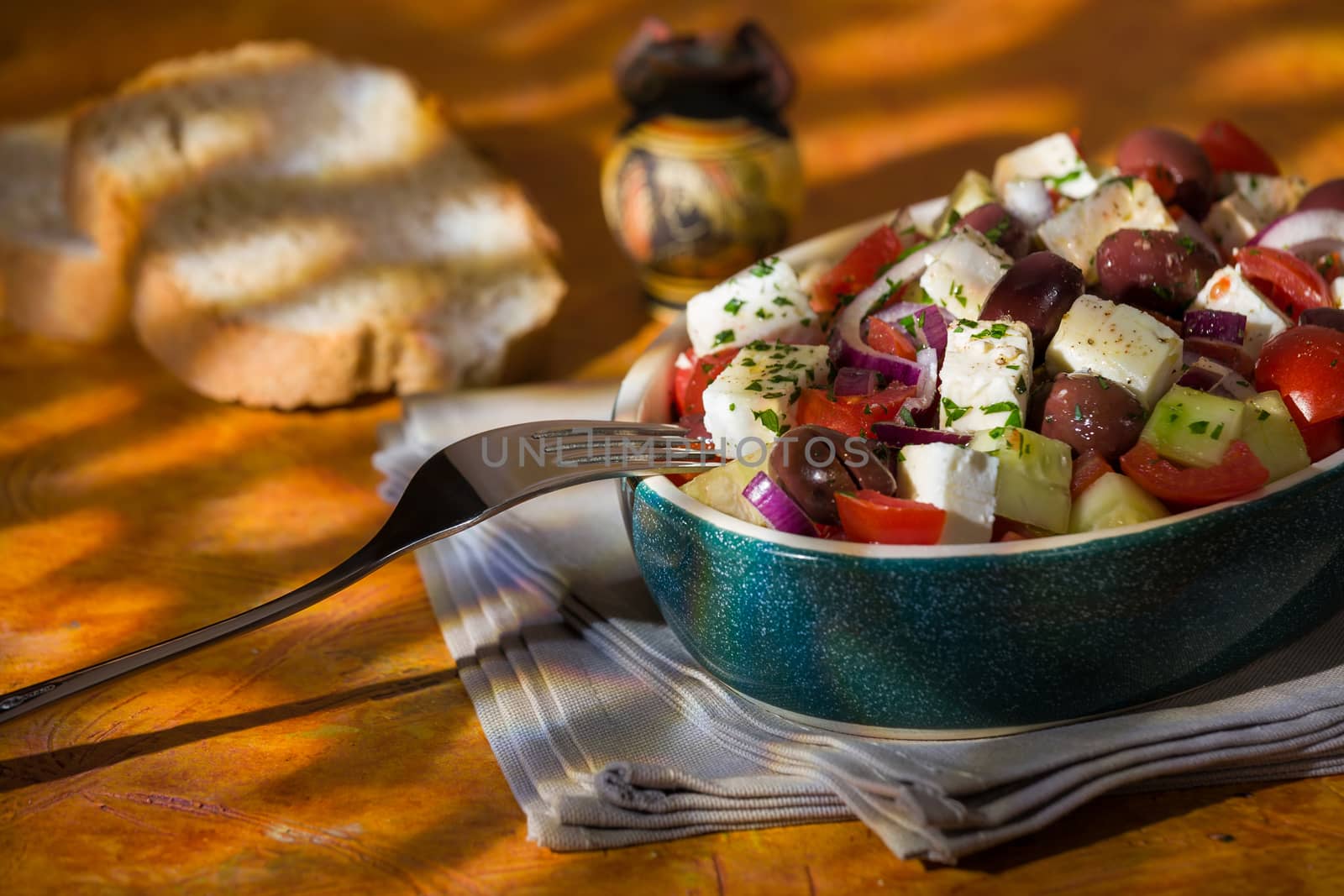 Greek salad with feta cheese tomatoes cucumber olives and onions with greek amphora and bread over a colored background