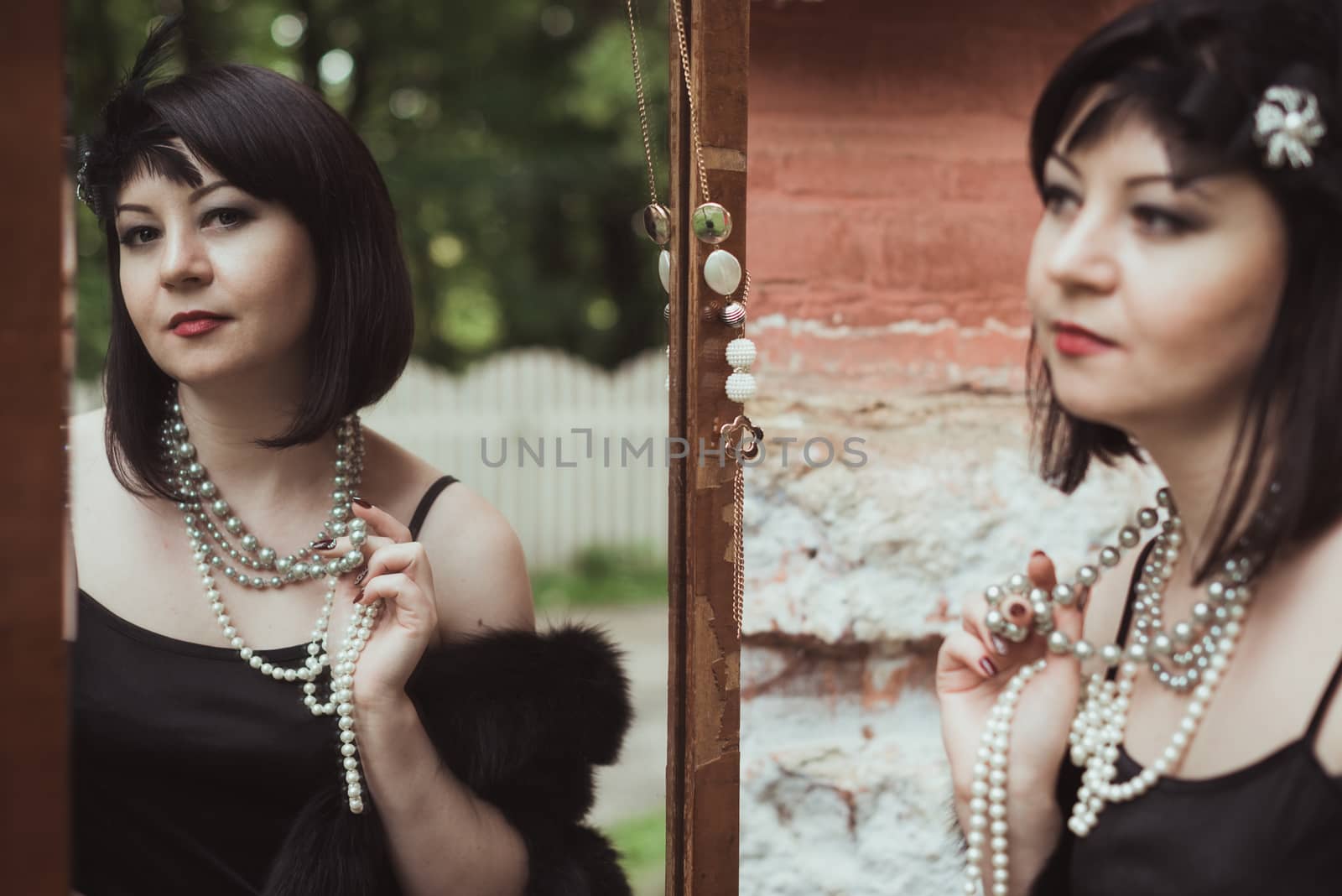 Portrait of a woman in retro style, looking in the mirror and holding a necklace