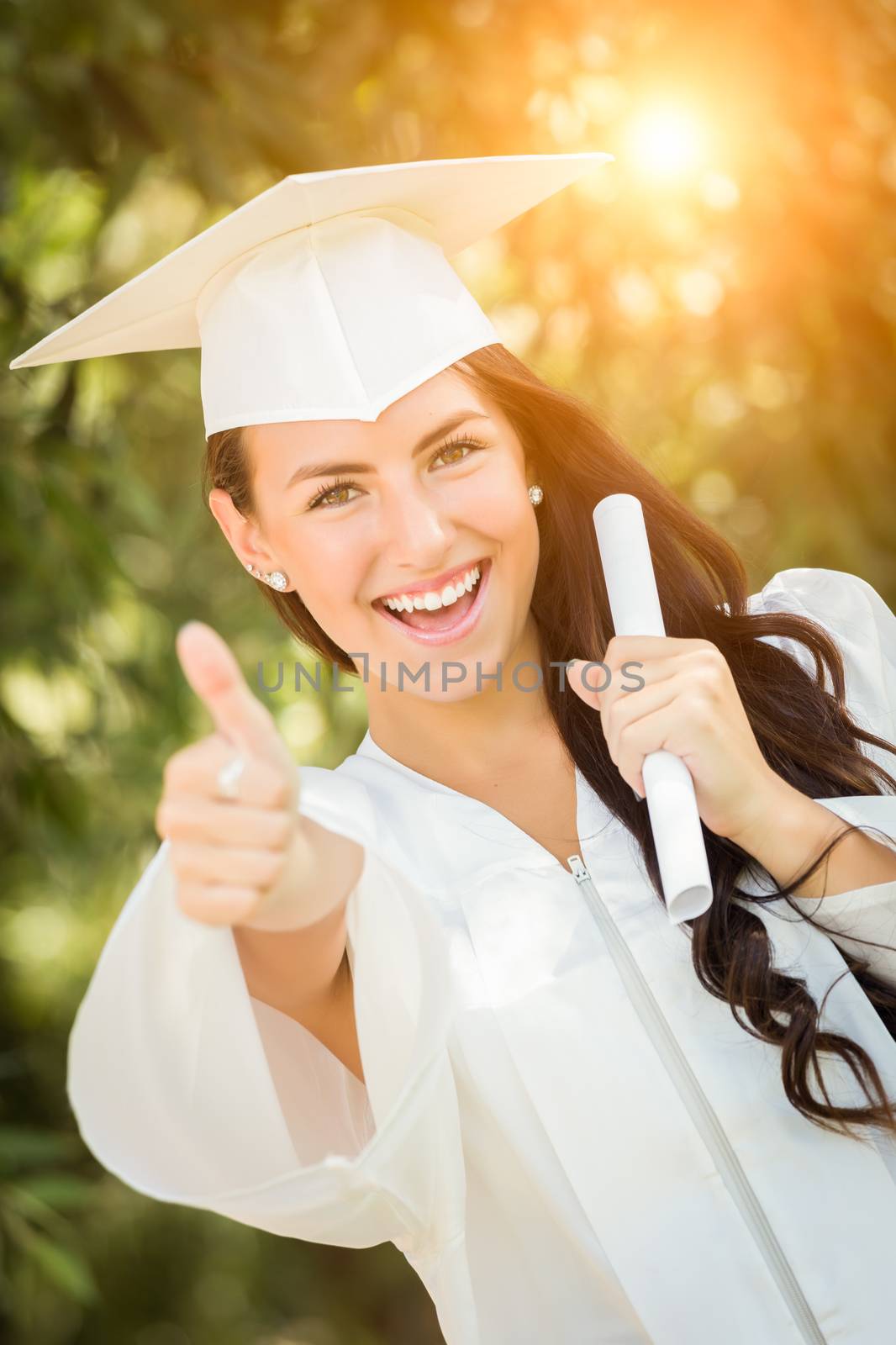 Attractive Mixed Race Girl Celebrating Her Graduation Outside In Cap and Gown with Diploma in Hand.