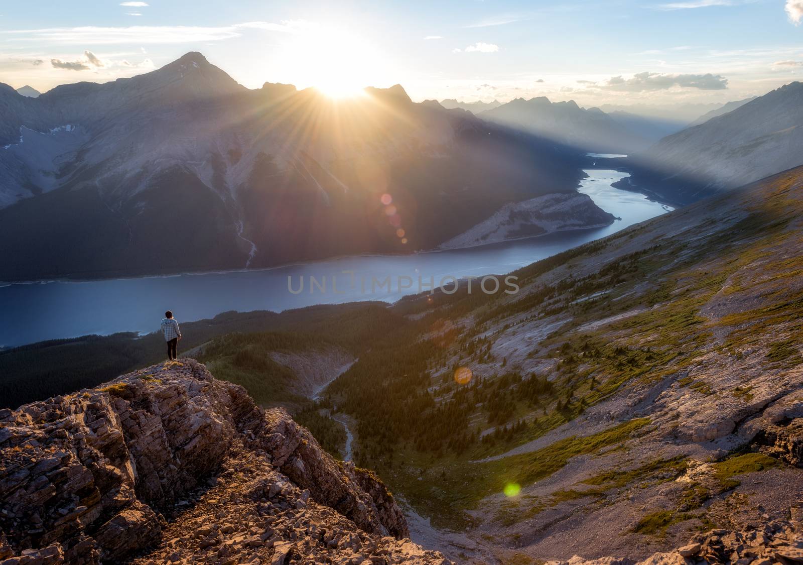Girl watching sunset from peak of mountain above a lake.