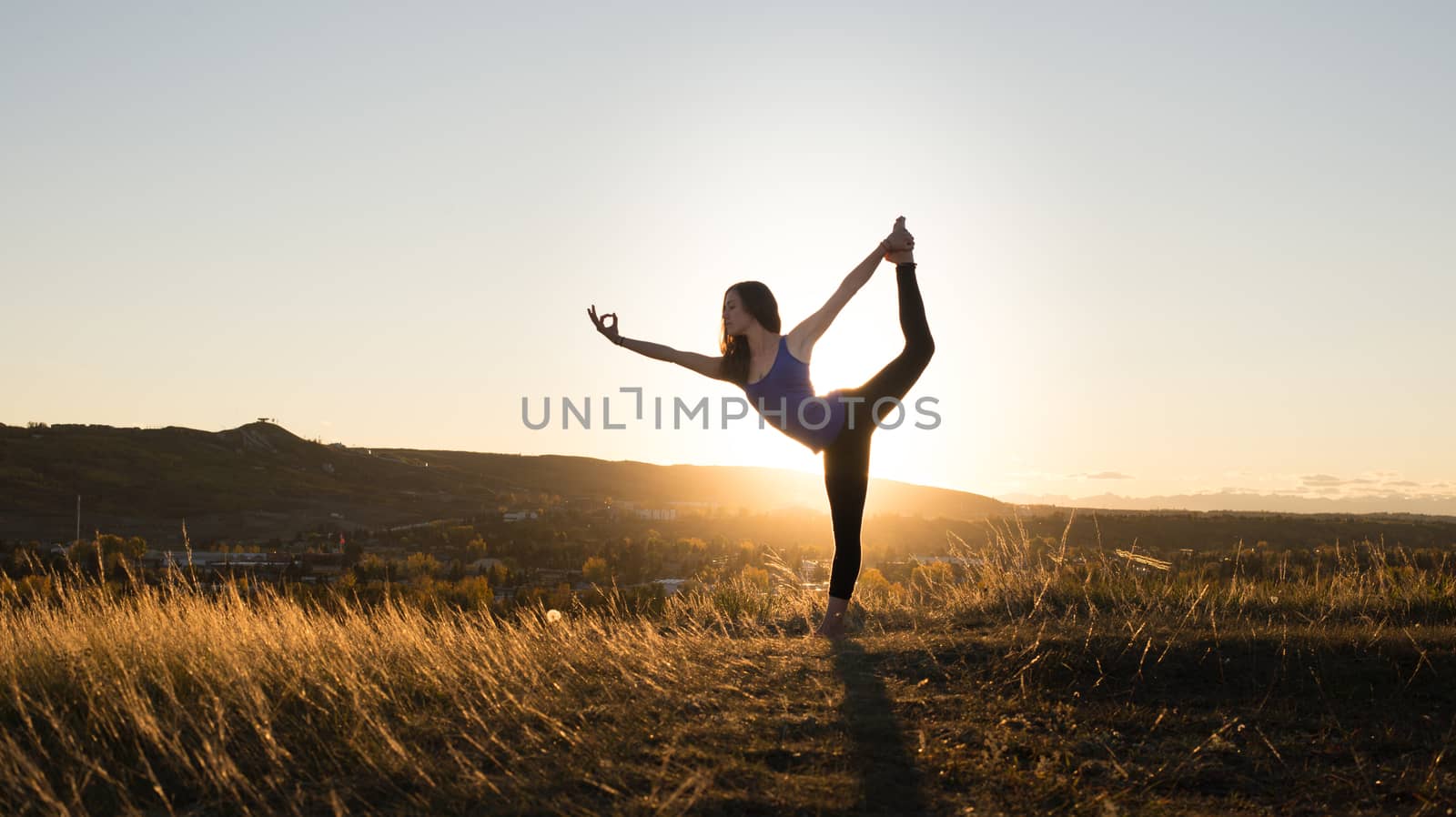Woman doing yoga dancers pose during sunset by TSLPhoto