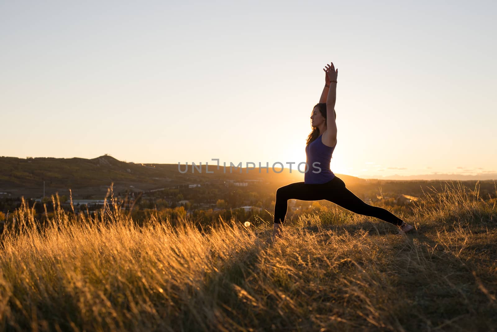 Woman doing yoga warrior I pose during sunset by TSLPhoto