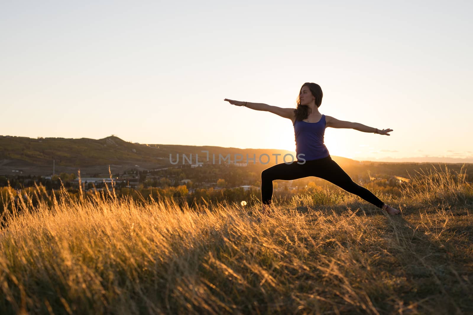 Woman doing yoga warrior II pose during sunset by TSLPhoto