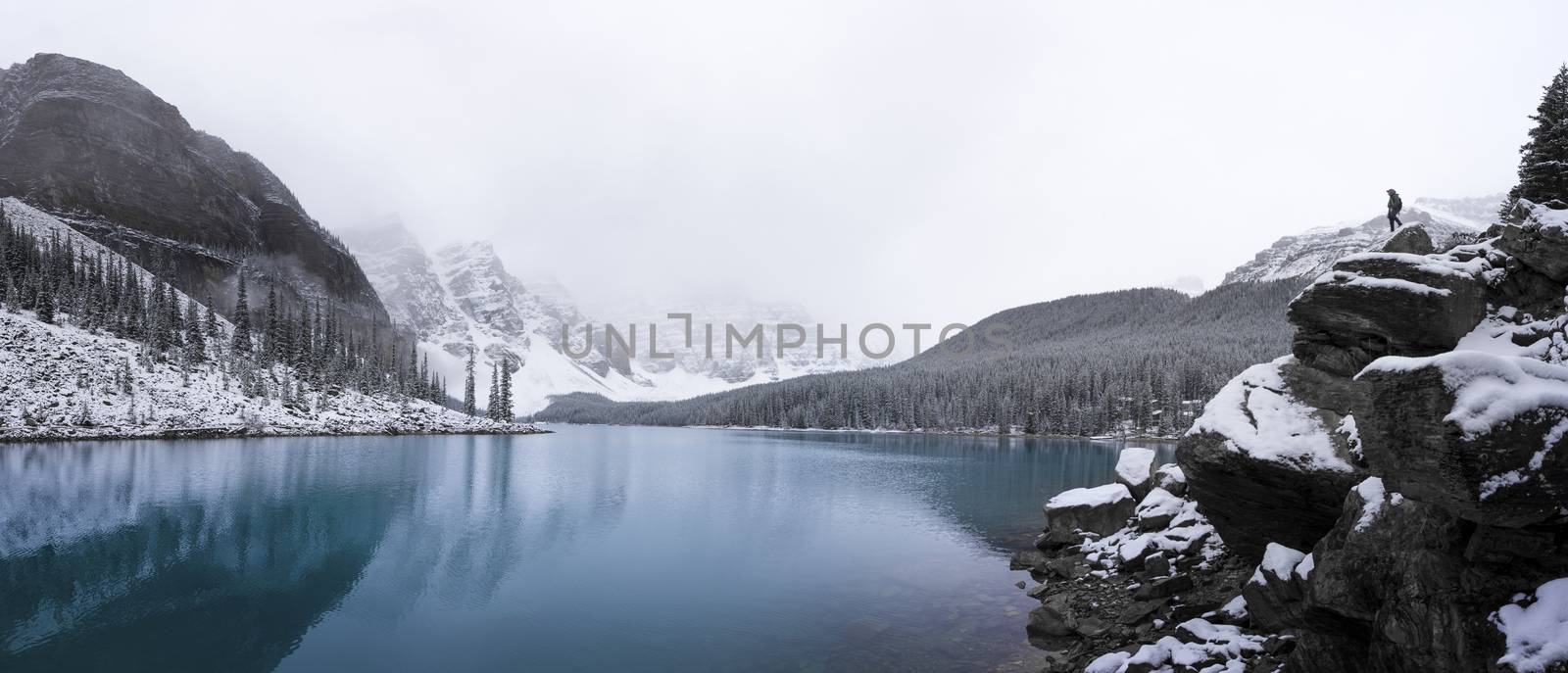 Panorama of Moraine lake after a fresh dusting of snow with man on rock