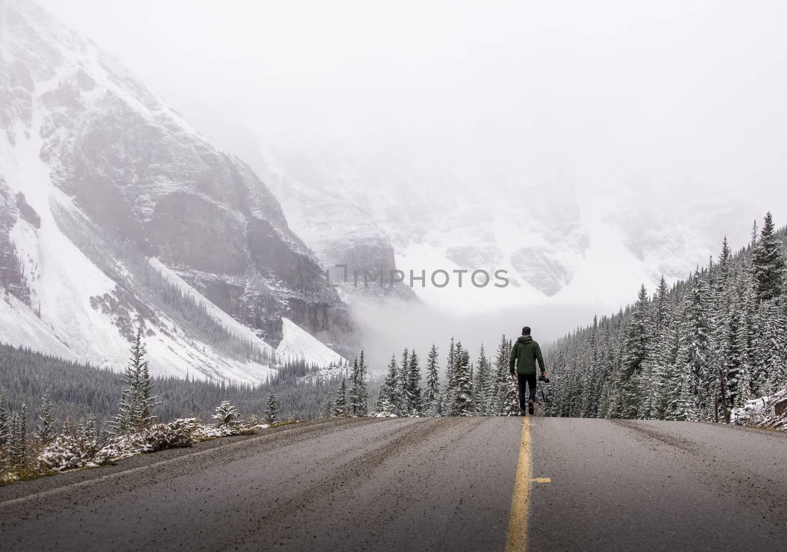 Photographer walks down a road in the winter holding his camera