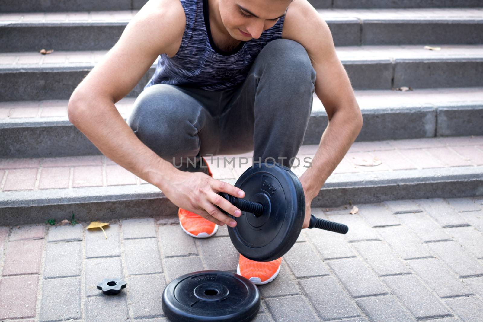 Young fintess man prepares dumbells for workout with weights outdoor