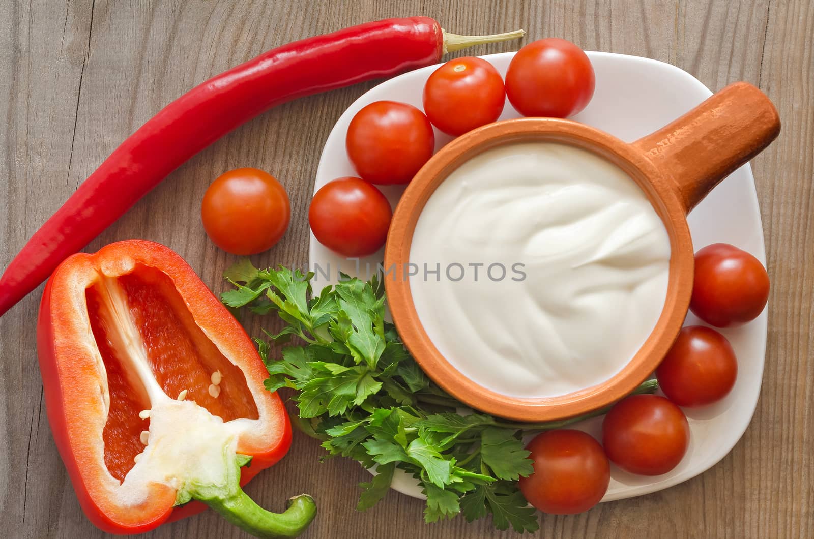 Ceramic dishes with sour cream, and ingredients for salad on an old wooden table.