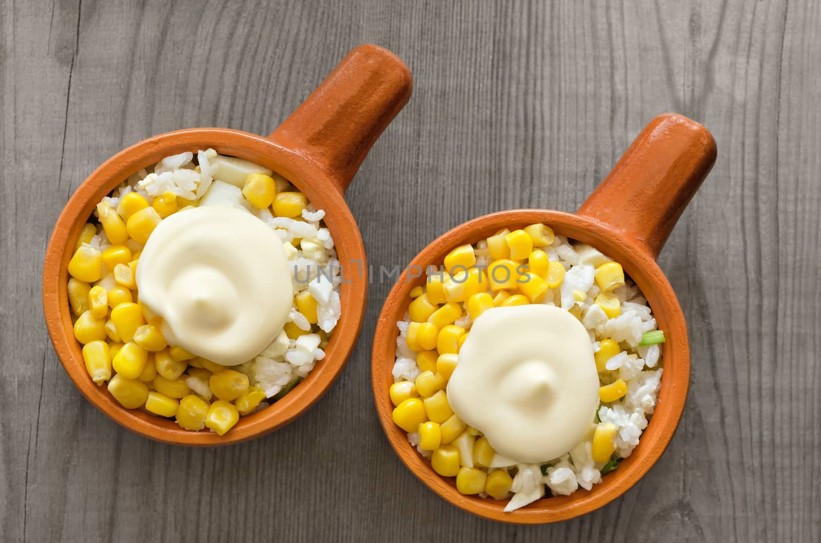 Rice salad and canned corn with mayonnaise, on a gray wooden background.