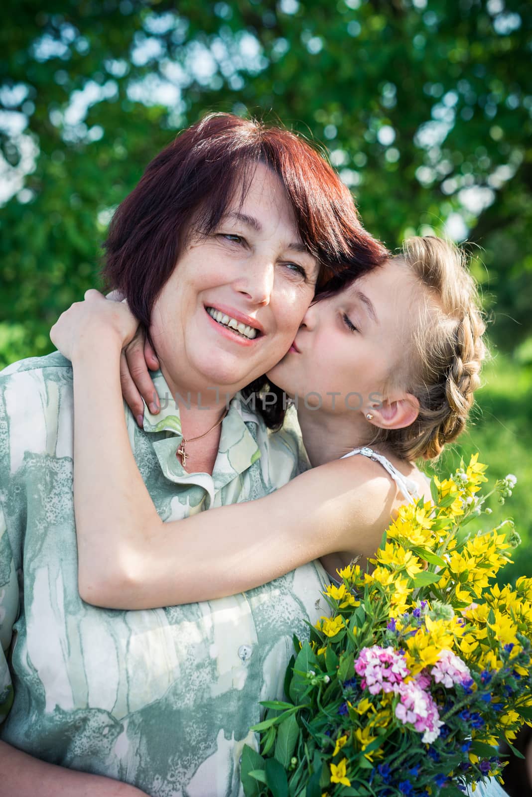 portrait of grandmother and granddaughter with flowers. Granddaughter kissing grandmother in the garden