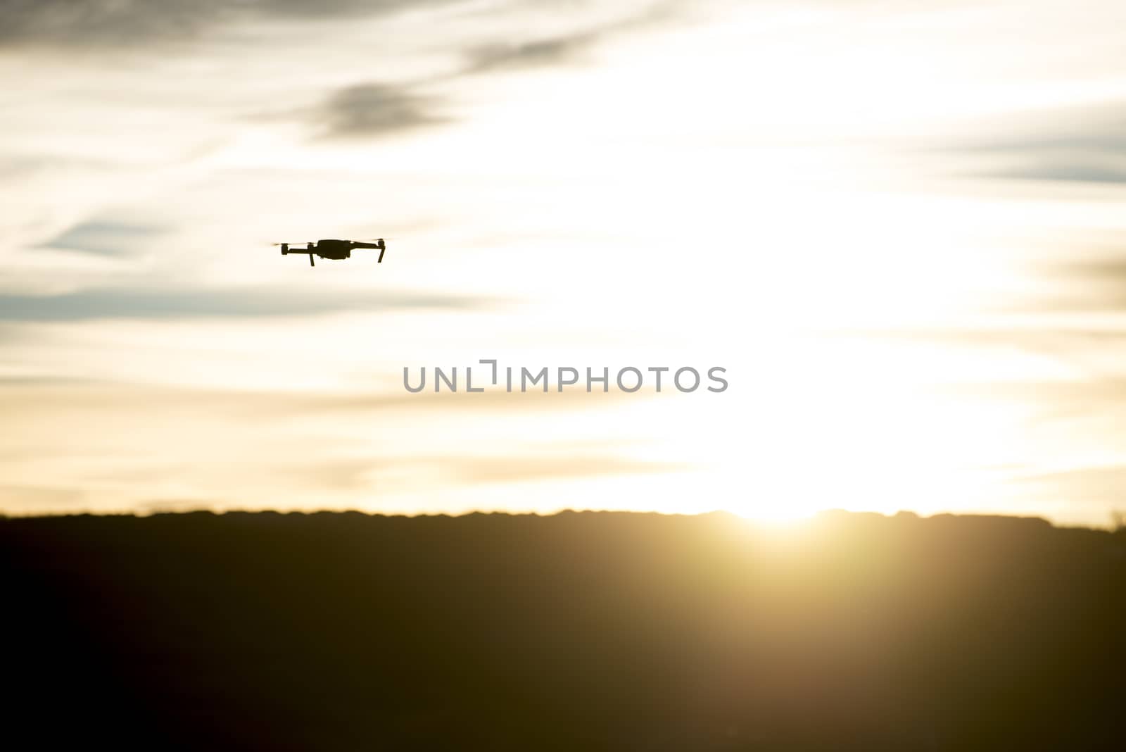 Small modern drone silhouetted against orange sunset taking video