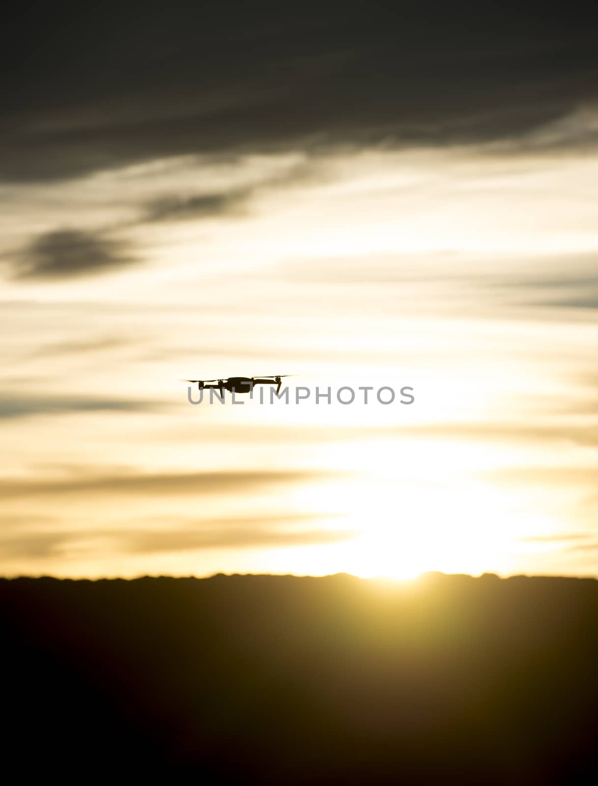 Small modern drone silhouetted against orange sunset taking video