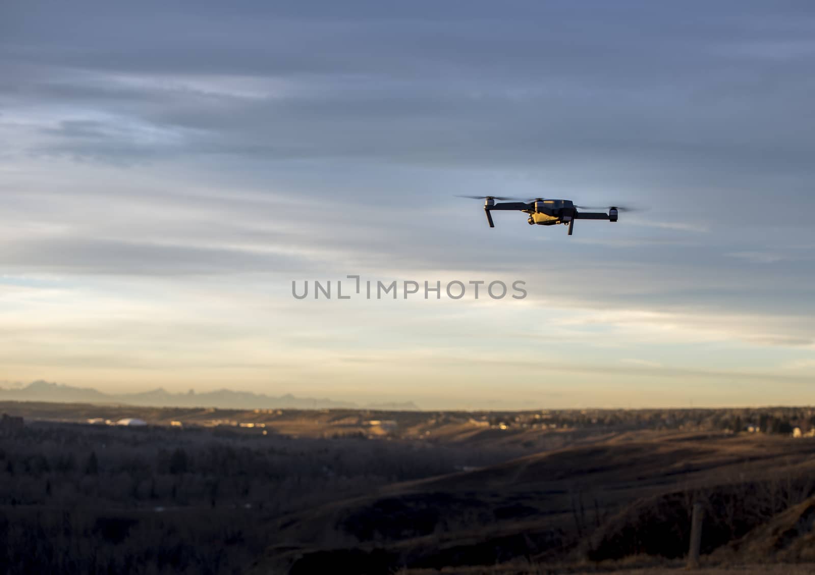 Small modern drone hovering taking picture of mountains at sunset