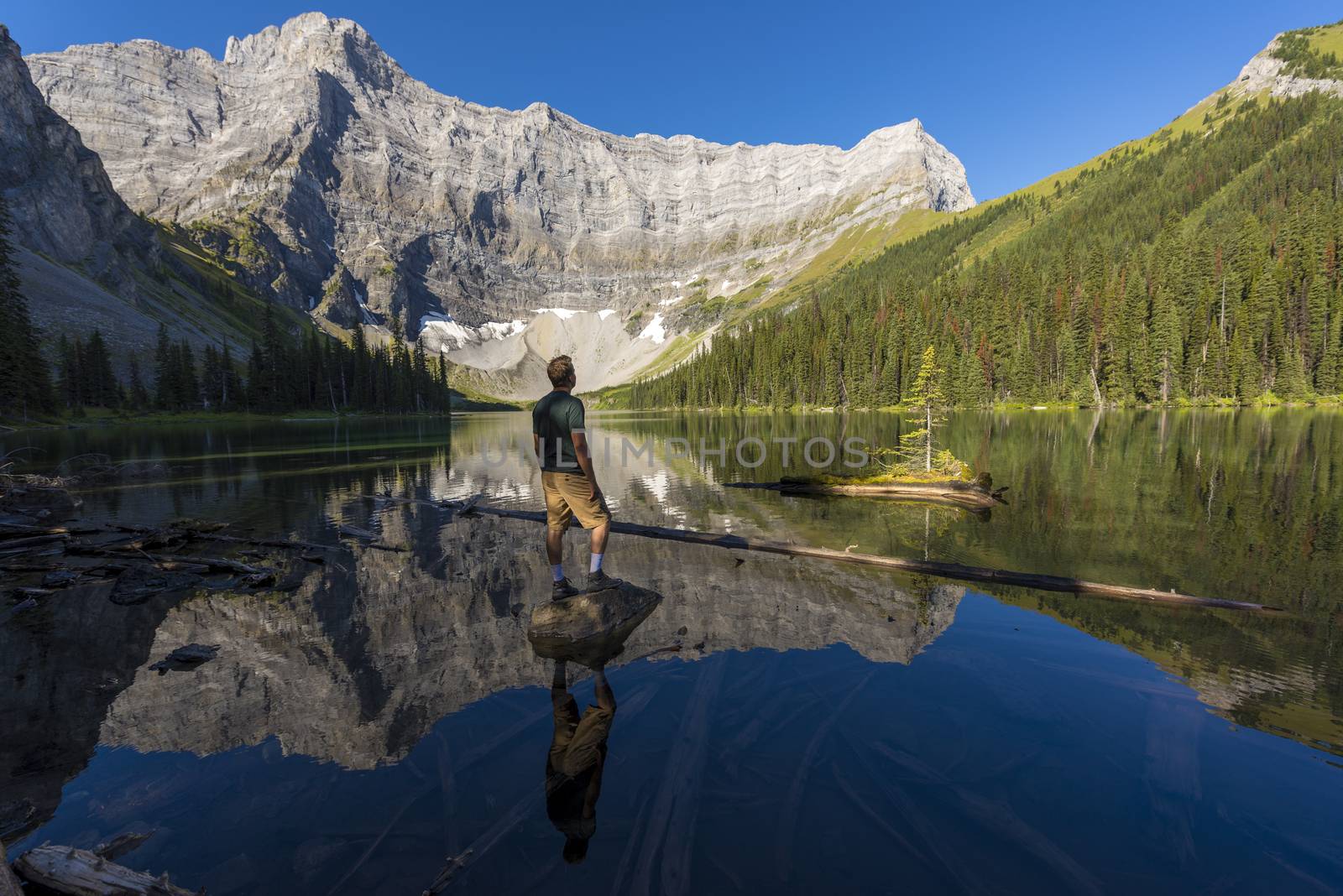 Young man standing on a rock in a lake looking up at mountains