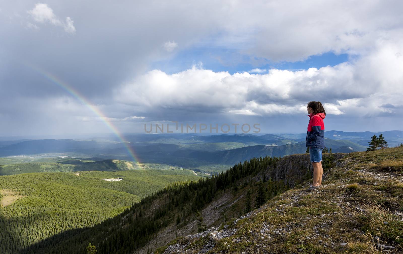 Young woman looks at rainbow from top of a hike